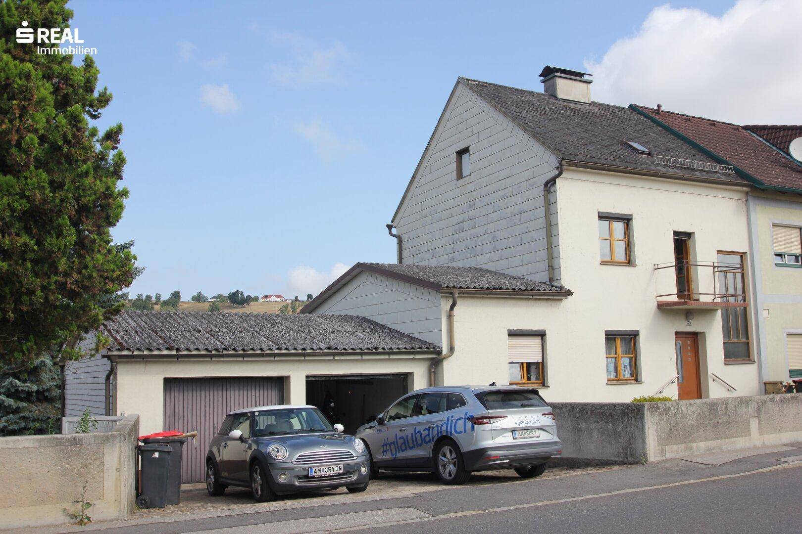 Seitenansicht des Hauses mit Garage und geparkten Autos an der Straße.