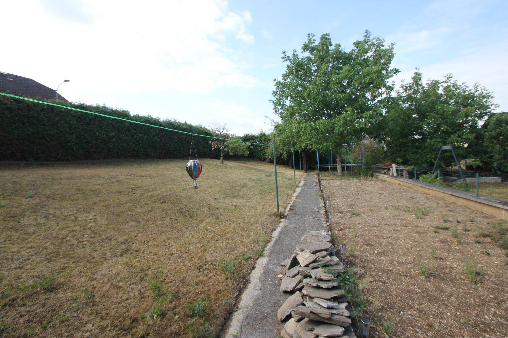 Weitläufiger Garten mit einem schmalen Pfad und einer Steinmauer am Rand.