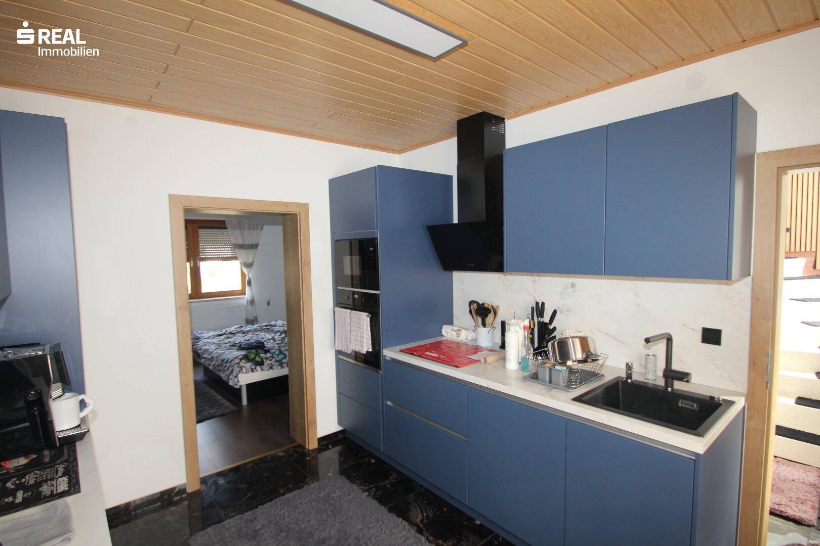 Moderne Küche mit blauen Schränken, dunklem Boden und Holzbalkendecke.