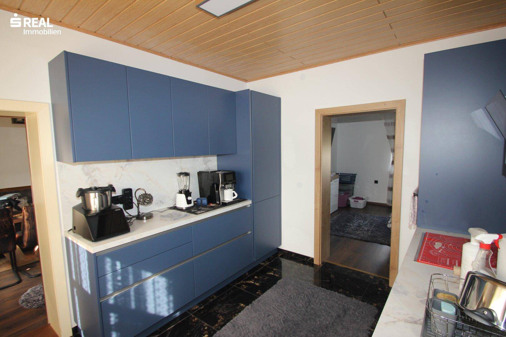 Helle Küche mit blauen Unterschränken, weißer Arbeitsplatte und Holzbalkendecke.
