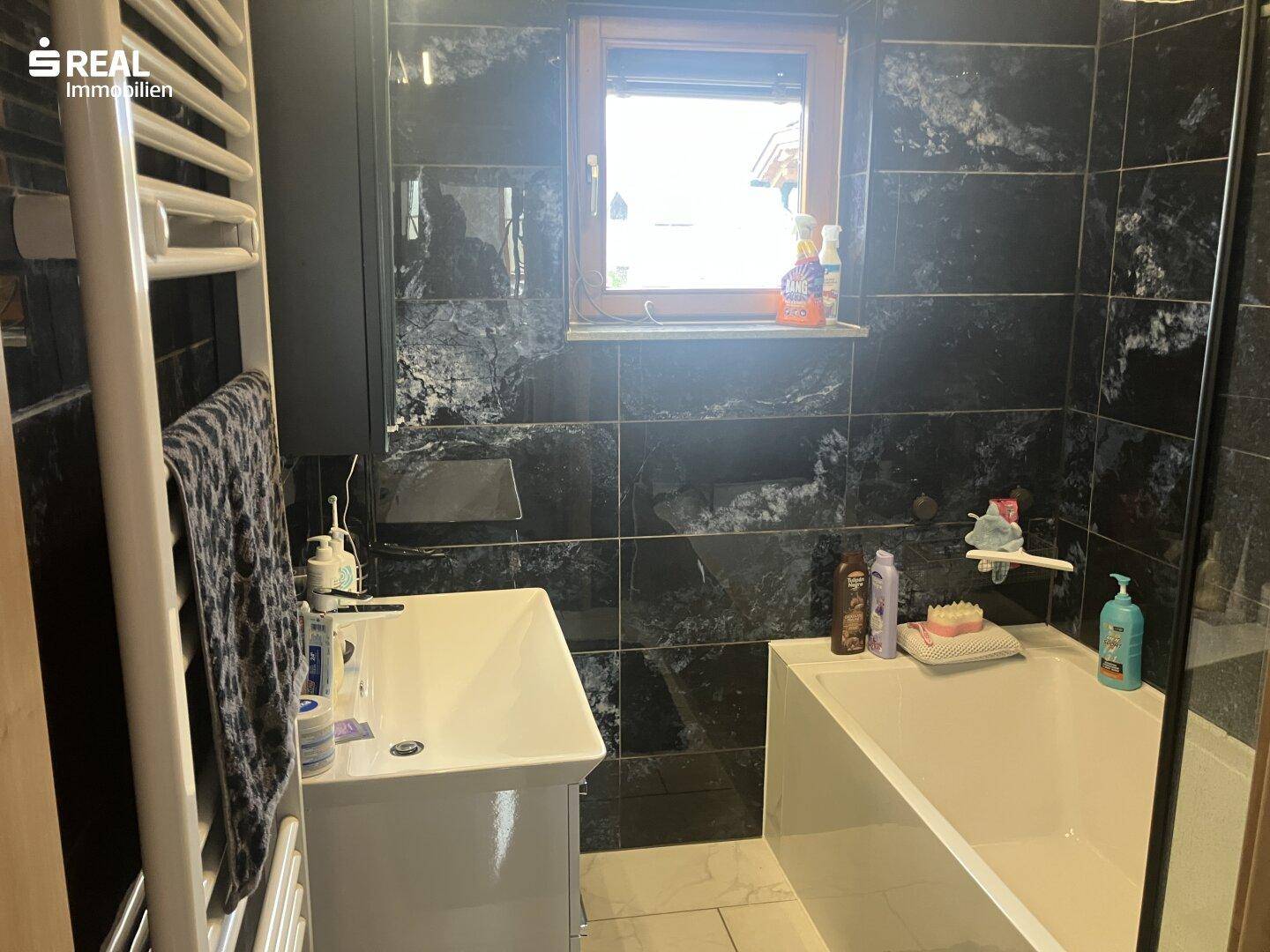 Modernes Badezimmer mit dunklen Fliesen, Badewanne und beheiztem Handtuchhalter.