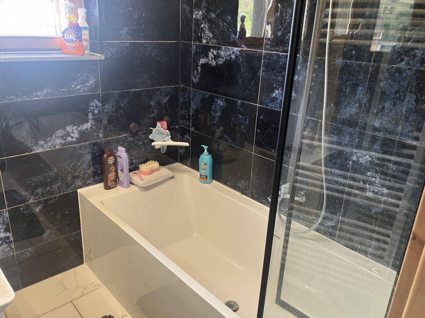 Elegantes Badezimmer mit dunklen Marmorfliesen, Badewanne und Duschbereich.