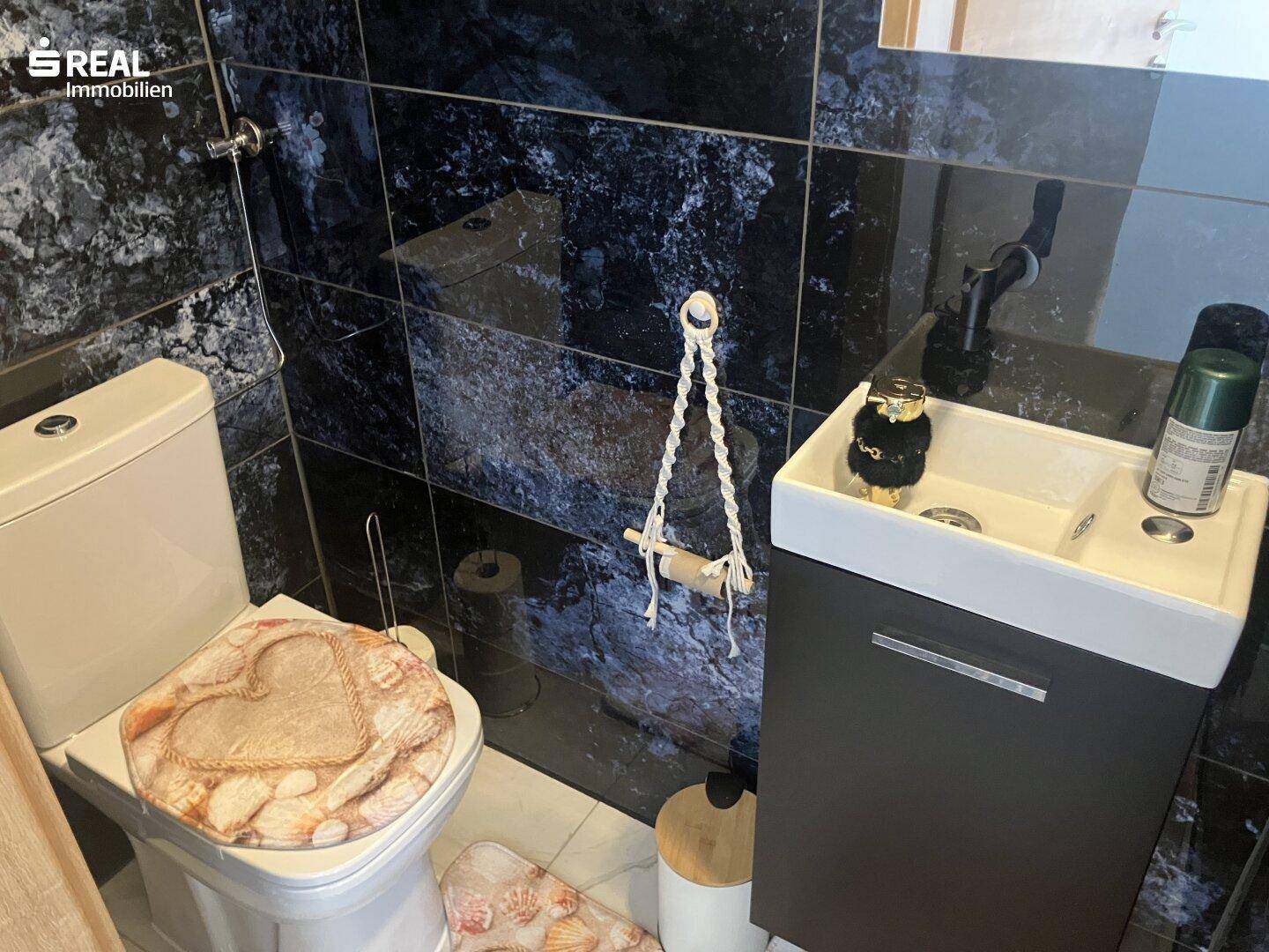 Kleines WC mit dunklen Fliesen, Toilette und Waschbecken.
