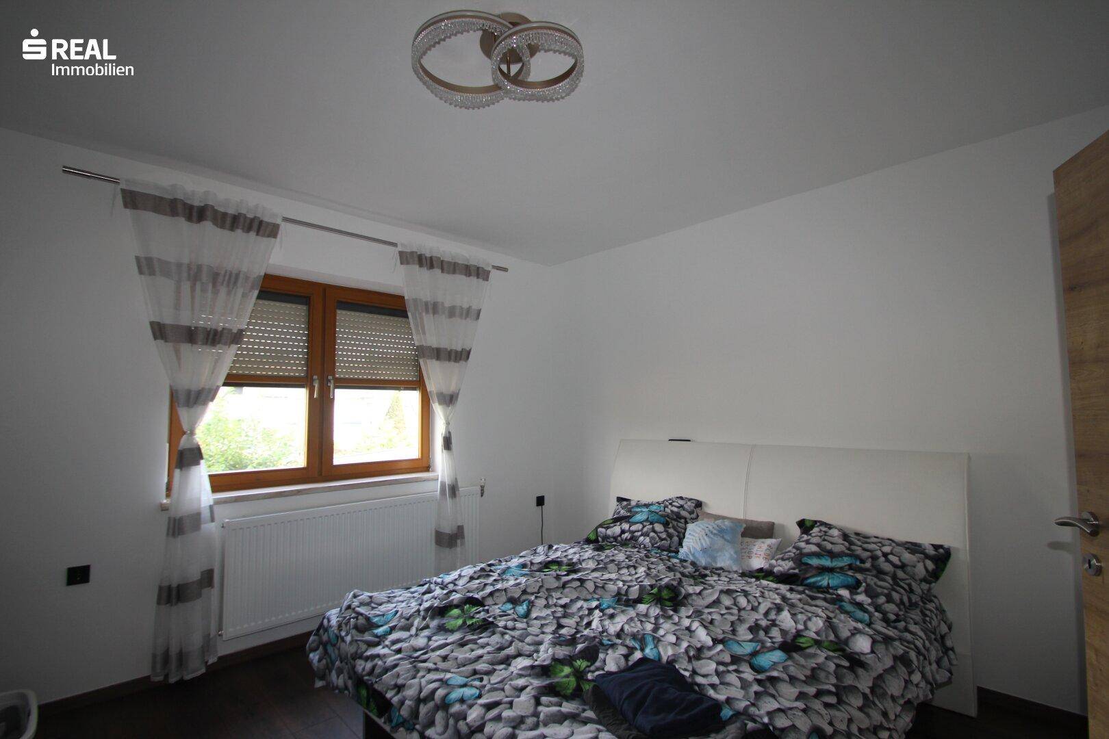 Helles Schlafzimmer mit großem Fenster, Doppelbett und dunklem Boden.