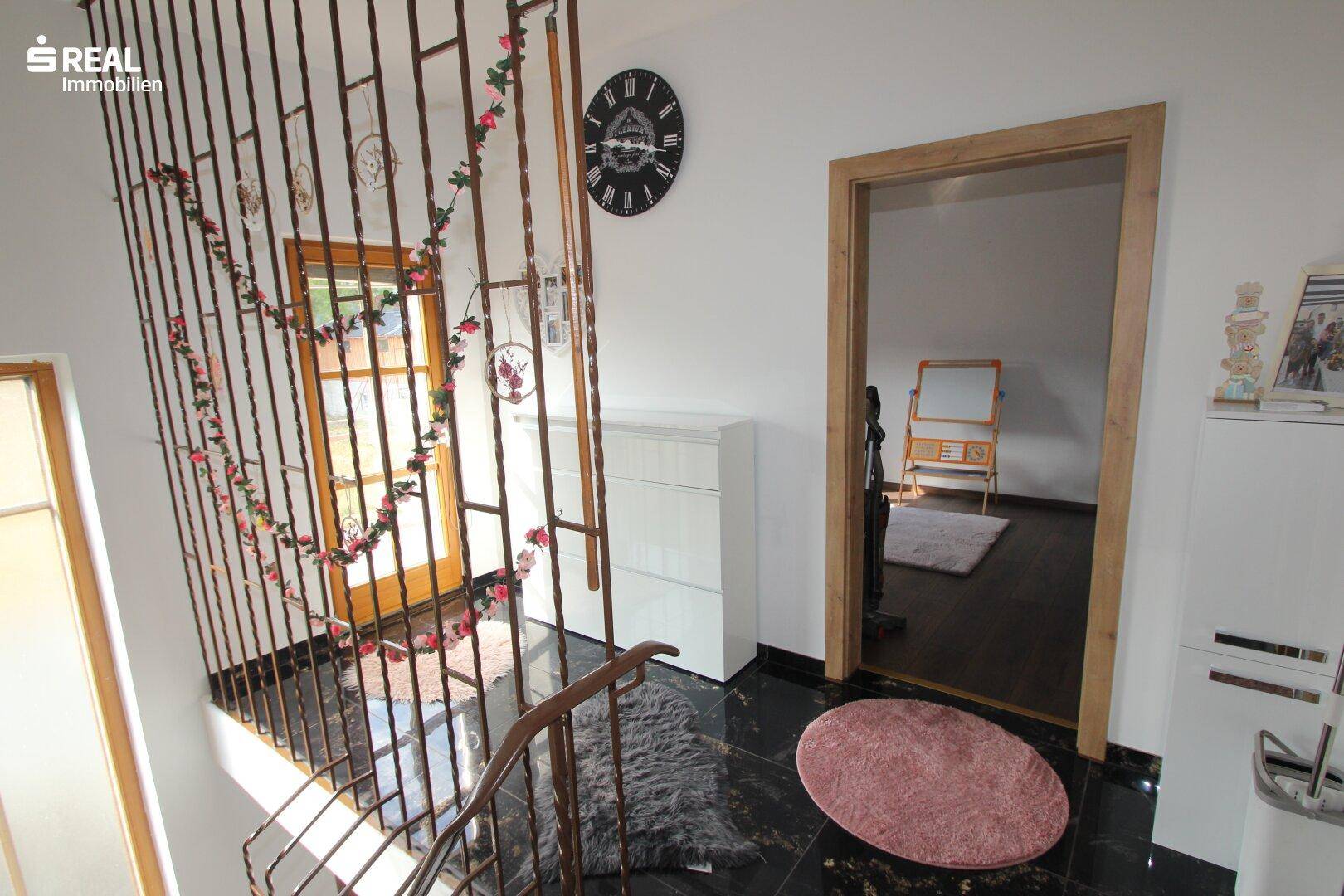 Heller Flur mit Treppengeländer, Fenster und Zugang zu einem weiteren Zimmer.