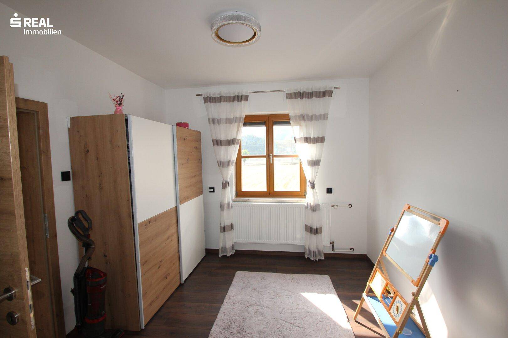Helles Zimmer mit Fenster, Kleiderschrank und Spieltafel.