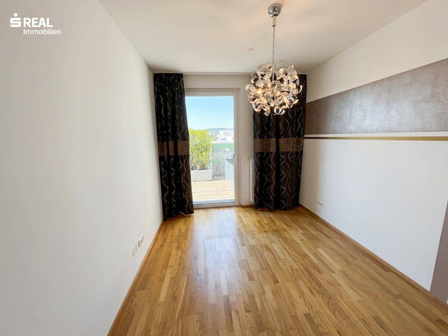 Schlafzimmer mit Parkettboden, Zugang zur Terrasse und dekorativen Vorhängen.