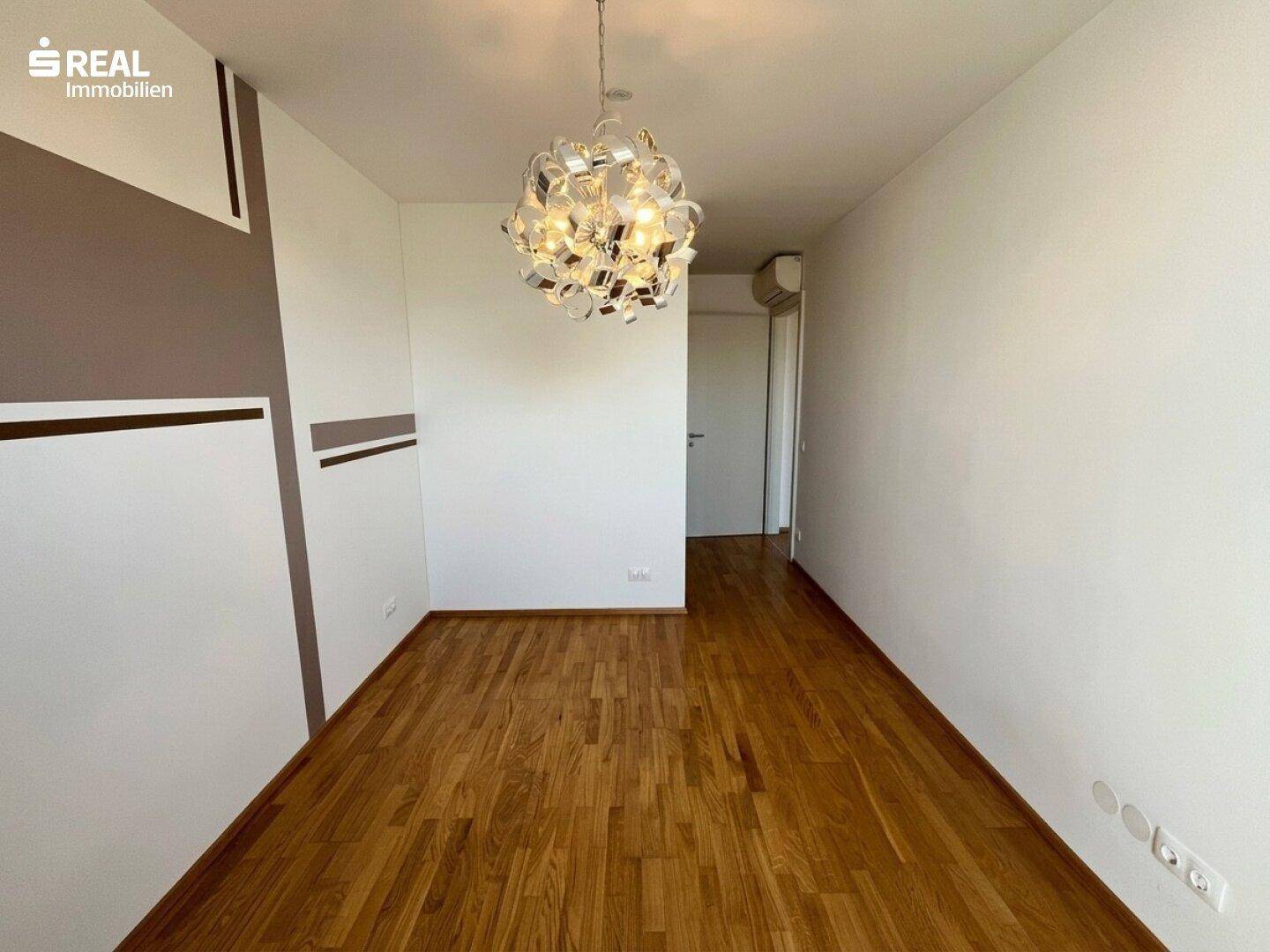 Geräumiges Schlafzimmer mit Holzboden und moderner Deckenleuchte.