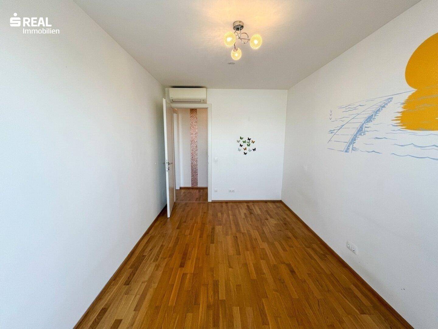 Kinderzimmer mit Holzboden und farbenfroher Wandmalerei, bietet viel Platz.