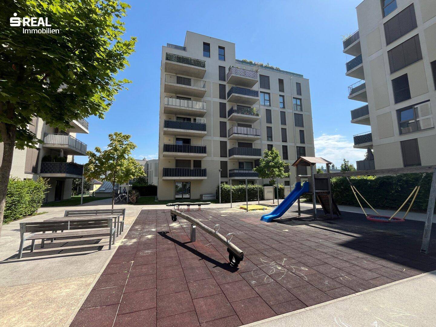 Moderner Spielplatz mit Rutsche und Schaukeln vor den Wohngebäuden.