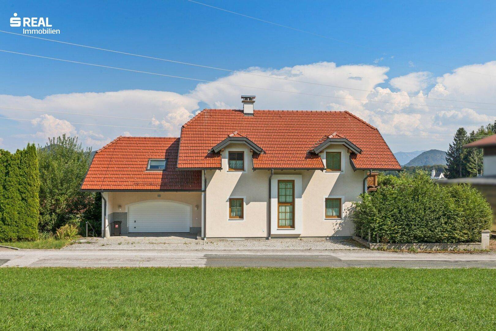Vorderansicht des Einfamilienhauses mit rotem Ziegeldach, Garage und gepflegter Hecke.