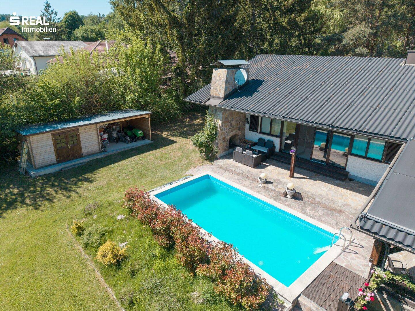 Luftaufnahme eines Hauses mit Pool, Garten und einem separaten Holzschuppen in ländlicher Umgebung.