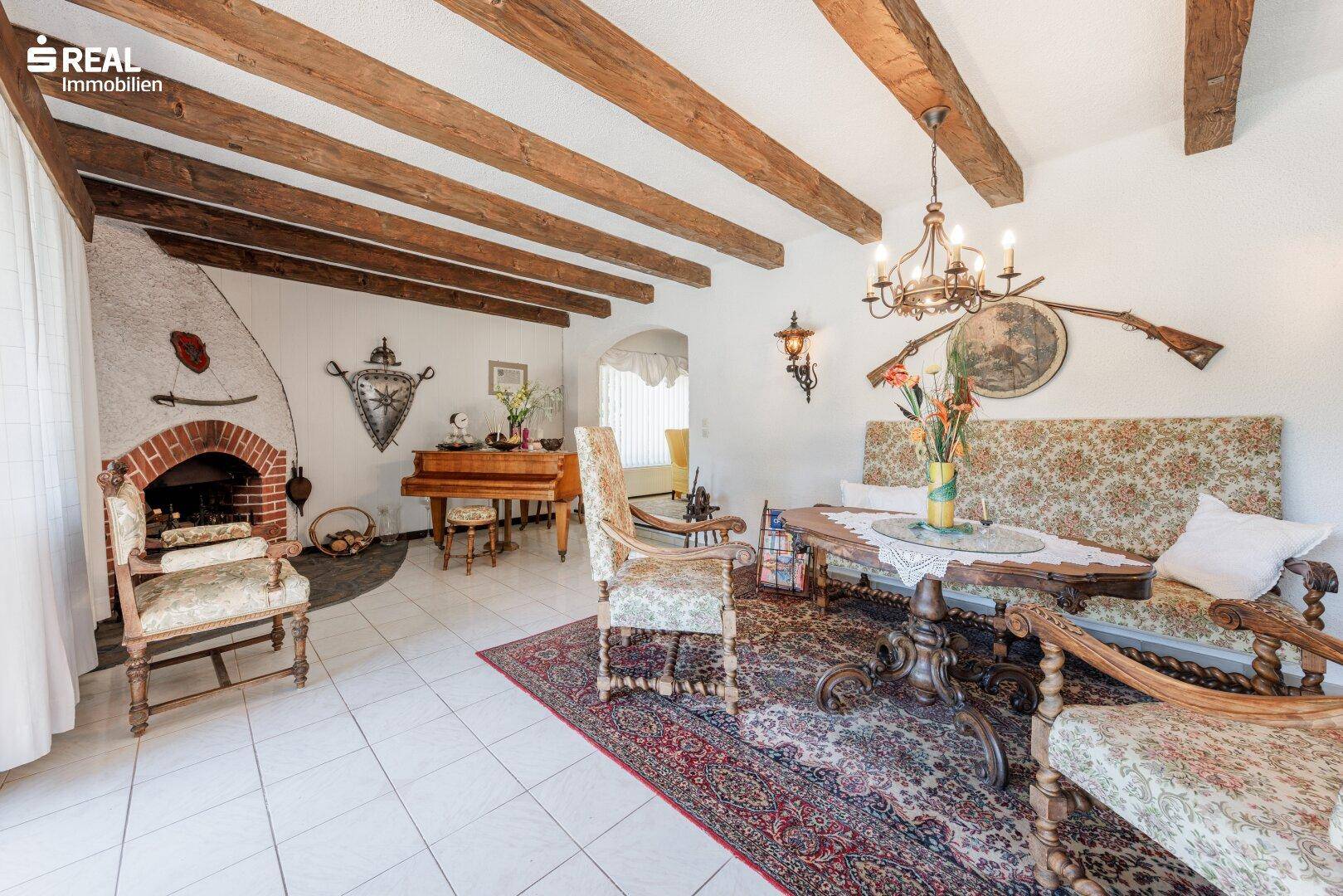 Gemütliches Wohnzimmer im Landhausstil mit sichtbaren Holzbalken, Kamin und traditionellen Möbeln.