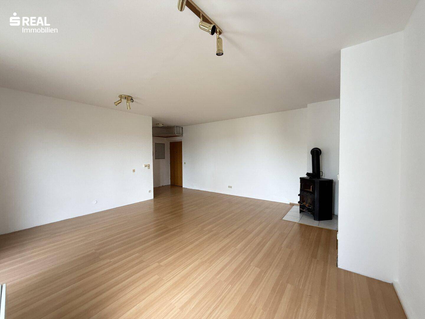 Geräumiges Wohnzimmer mit hellem Holzboden und einem gemütlichen Holzofen, bereit zur individuellen Gestaltung.