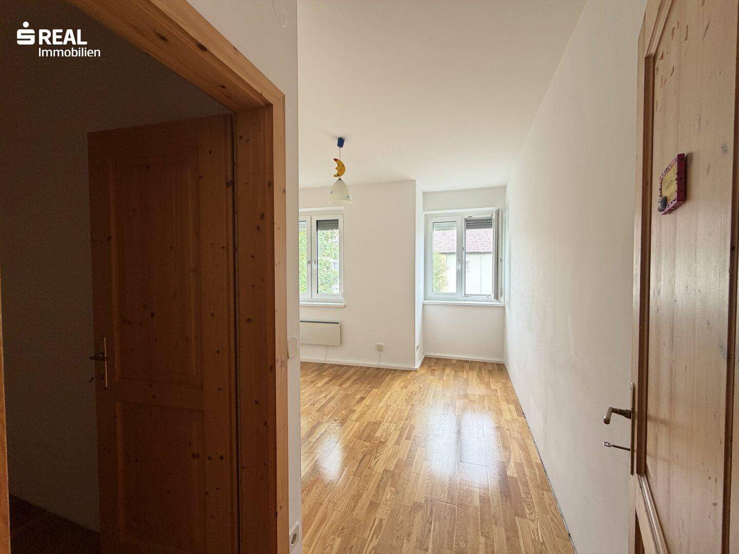 Heller Flur mit Holztüren, der zu einem weiteren Zimmer mit Parkettboden führt.