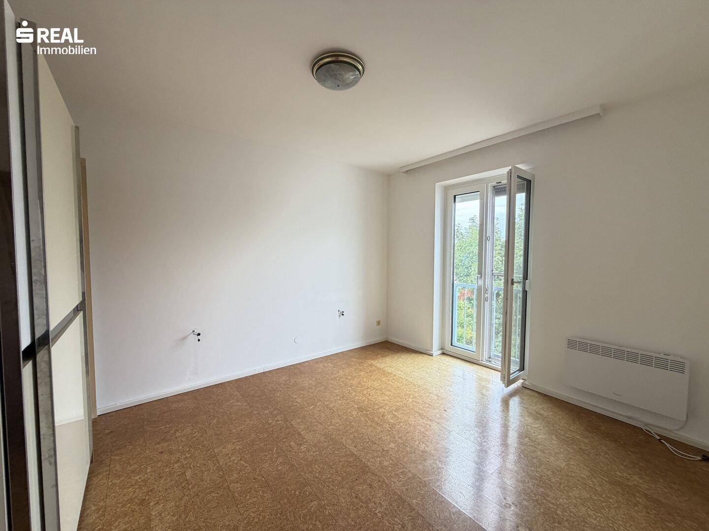 Helles Zimmer mit Korkboden und Zugang zu einem französischen Balkon, bietet viel Tageslicht.