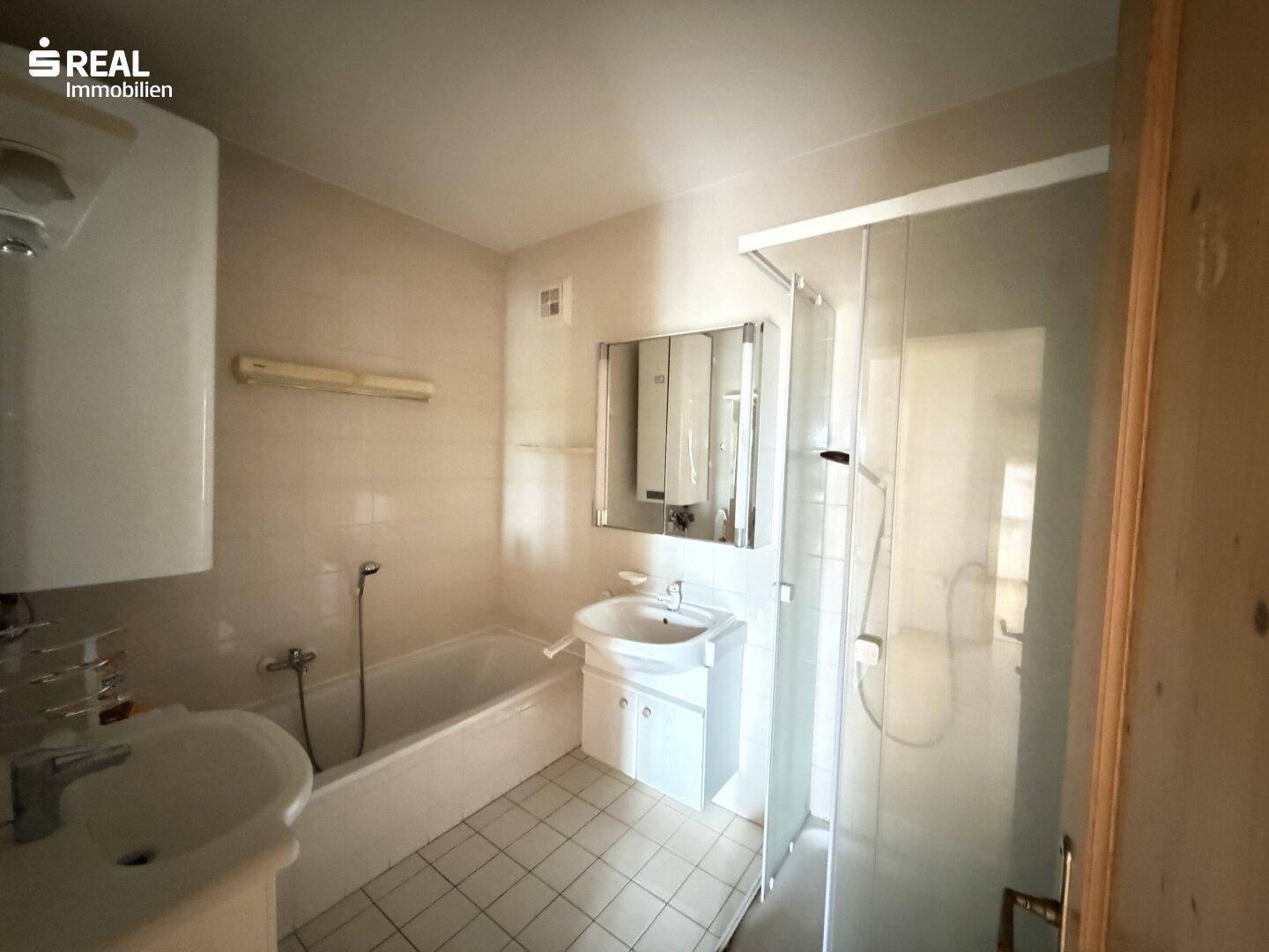 Funktionales Badezimmer mit Badewanne, Duschkabine, Waschbecken und hellen Fliesen.