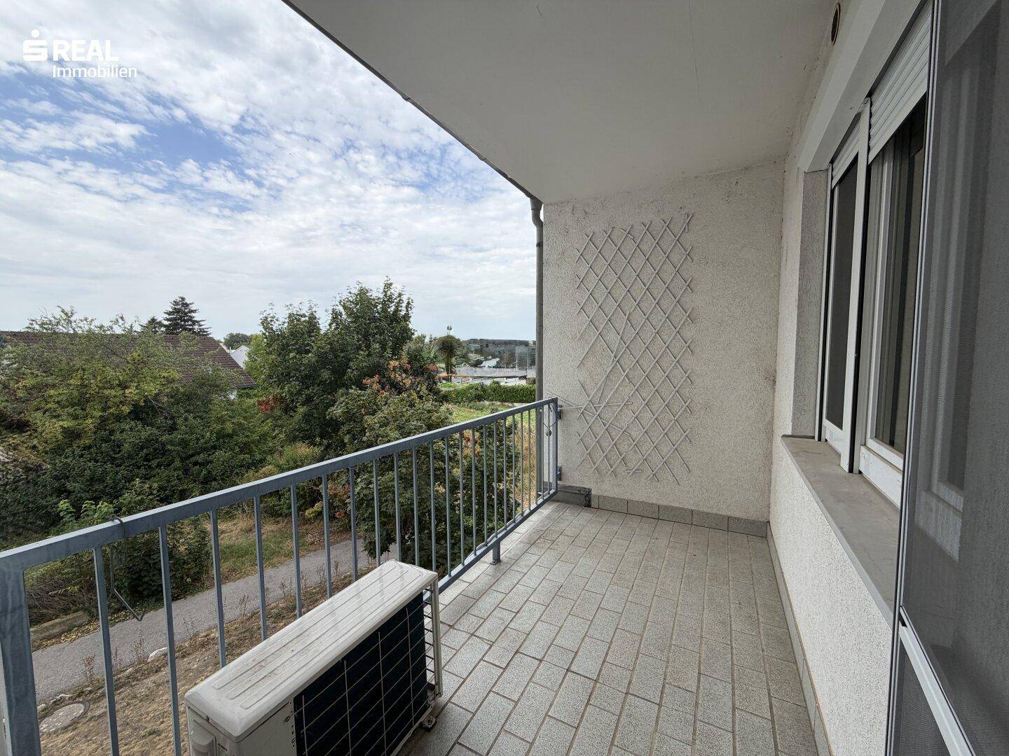 Balkon mit Fliesenboden und Metallgeländer, bietet einen Ausblick ins Grüne und auf die Umgebung.