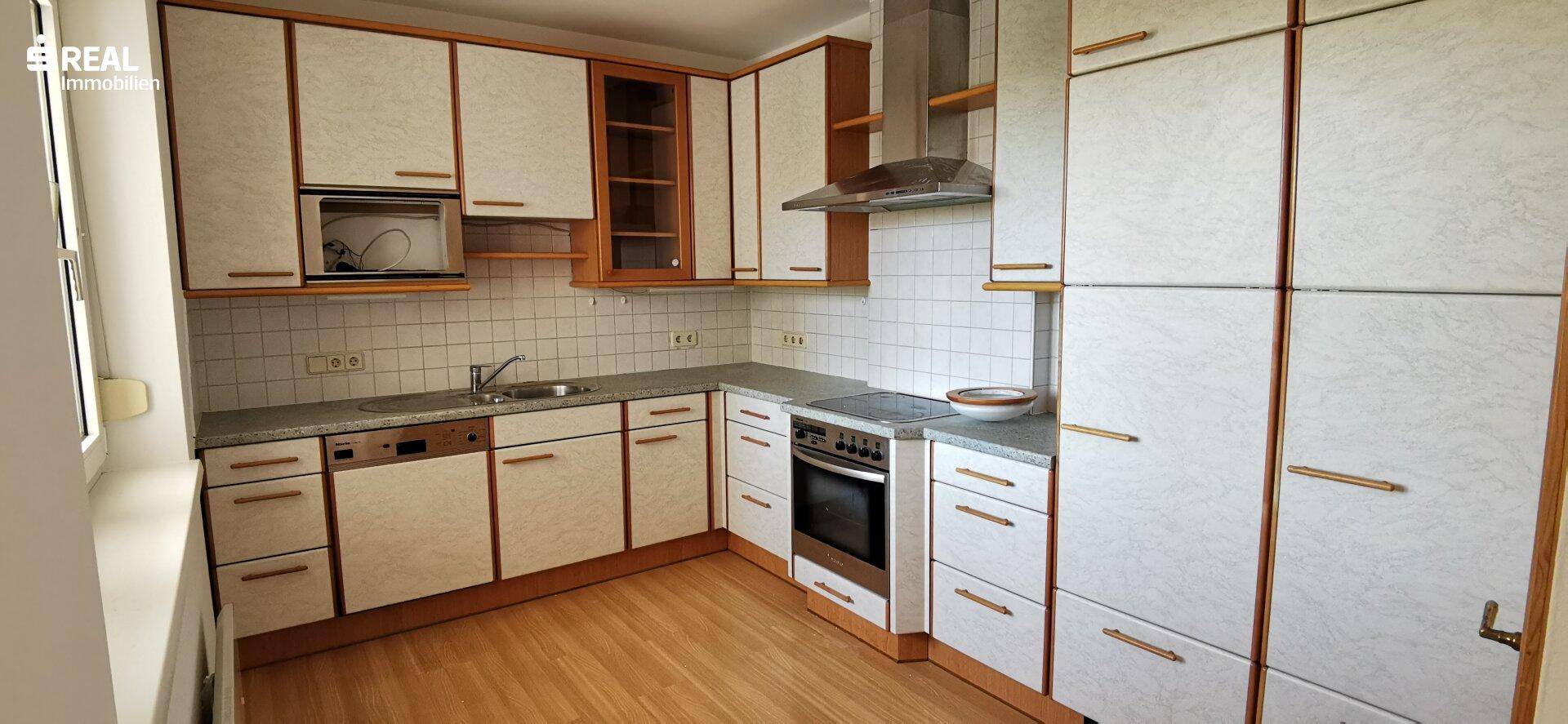Funktionale Küche mit weißen Schränken, Holzdetails, Fliesenrückwand und integrierten Geräten.
