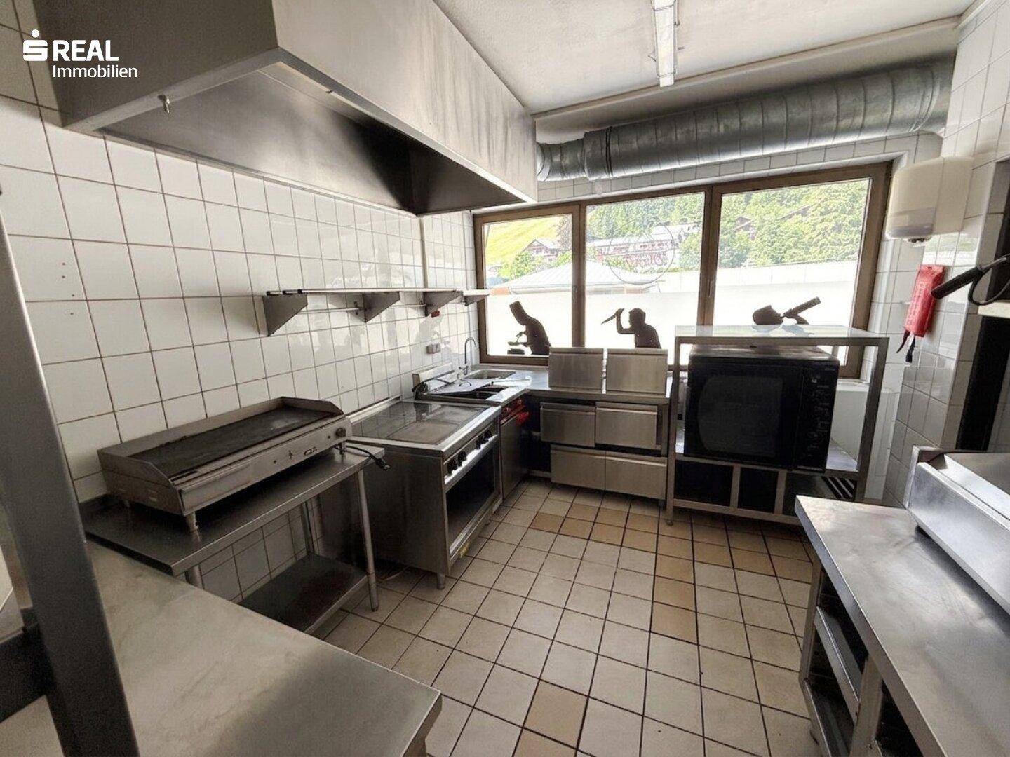 Professionelle Gewerbeküche mit Edelstahloberflächen, großer Dunstabzugshaube und Kochgeräten.
