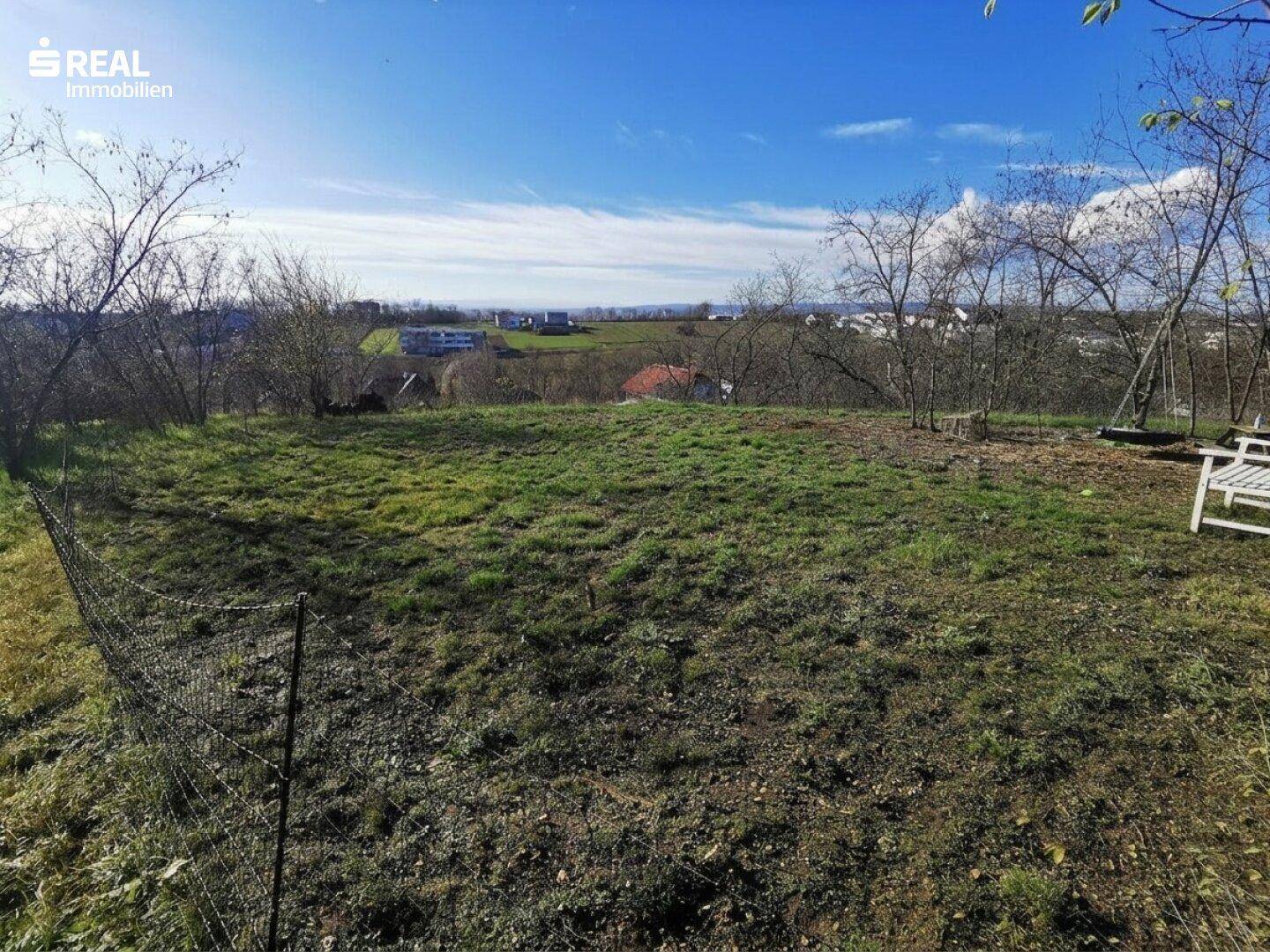 Weitläufiges Gartengrundstück mit Blick auf die umliegende Bebauung und grüne Hügel.