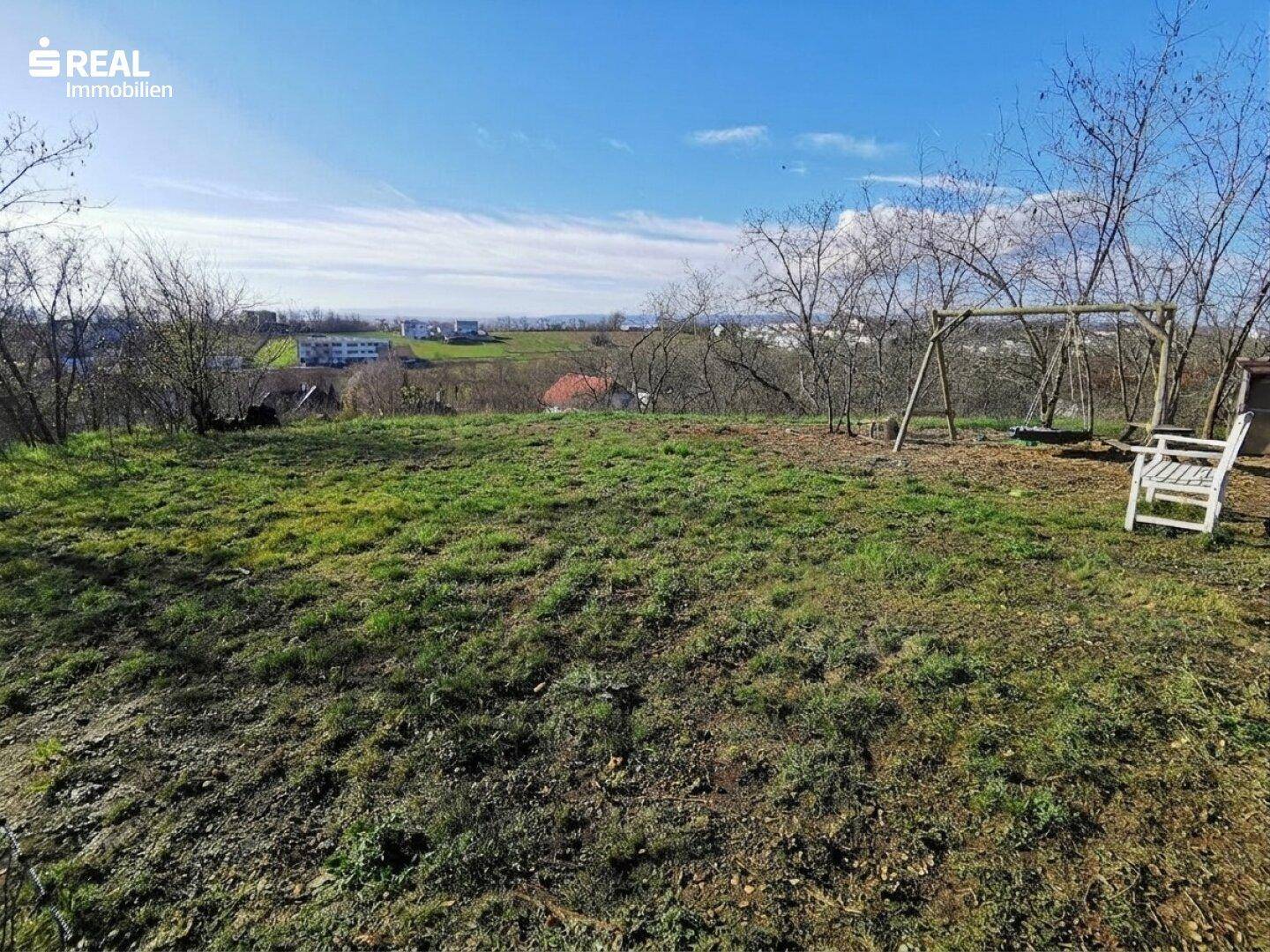 Weitläufiges Gartengrundstück mit Schaukel und Sitzbank, umgeben von Natur und Fernblick.