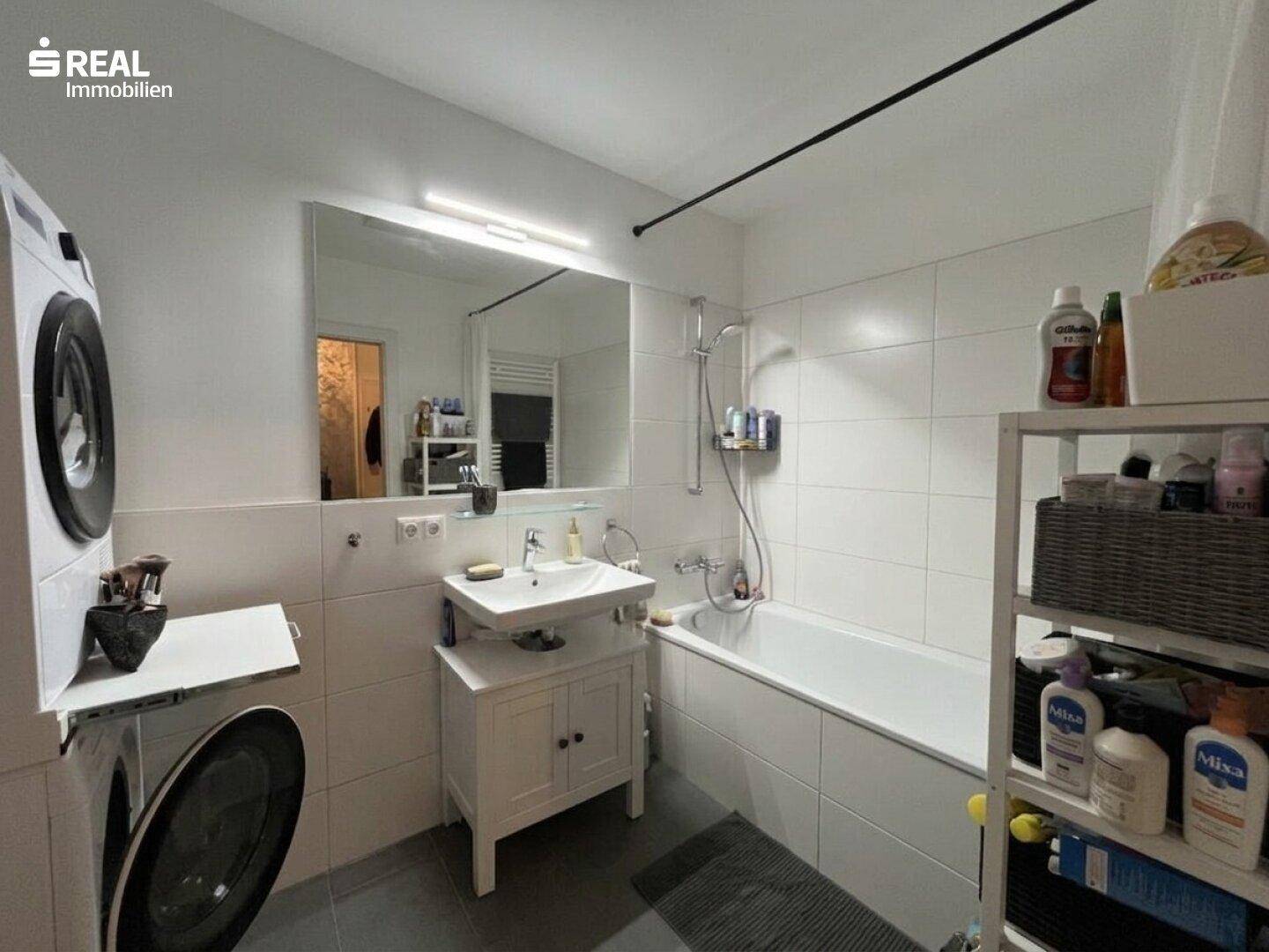 Modernes Badezimmer mit Badewanne, Waschbecken und integrierter Waschmaschine.