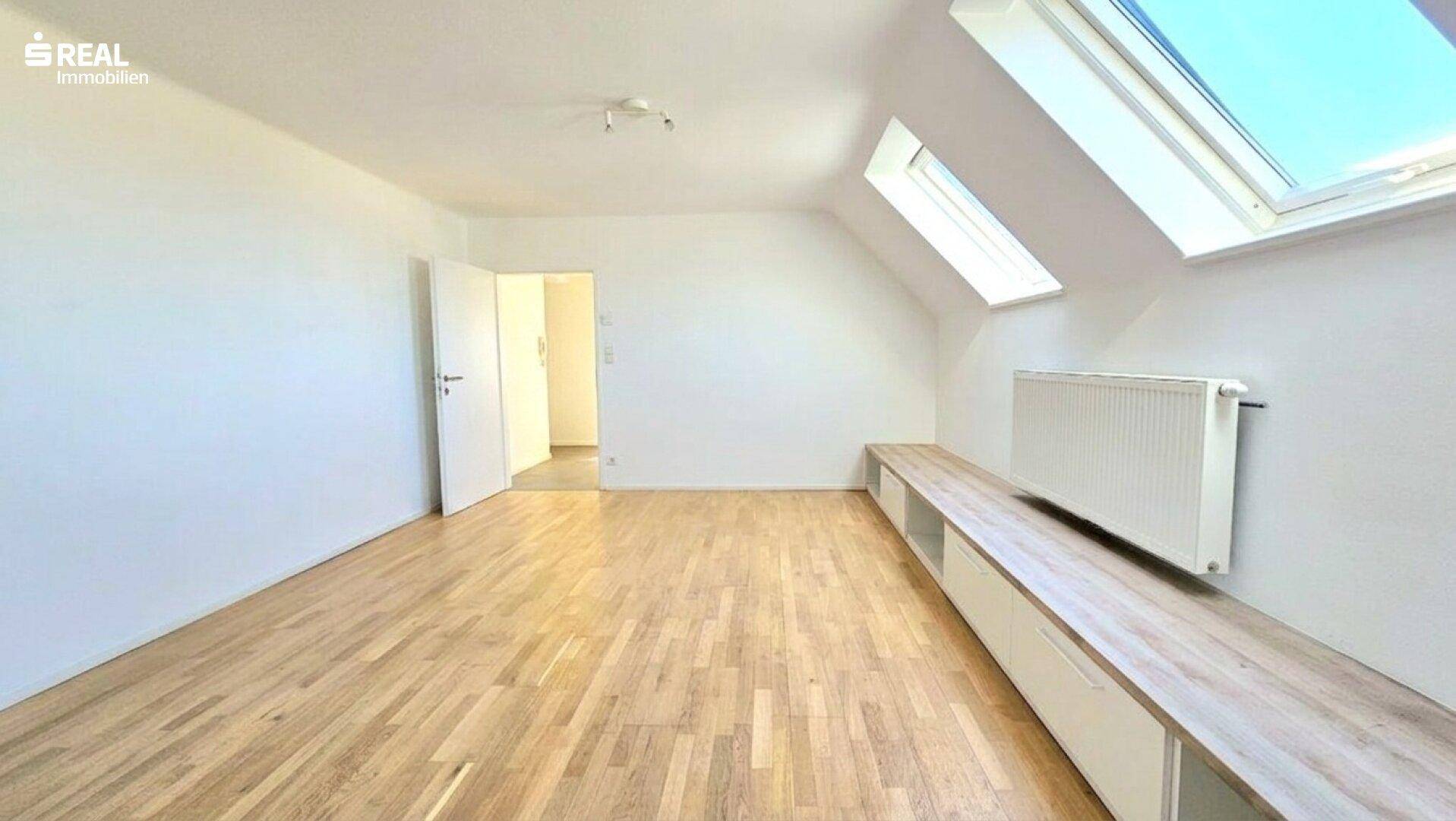 Geräumiger Wohnbereich mit hellem Parkettboden, Dachschrägen und großem Dachfenster.