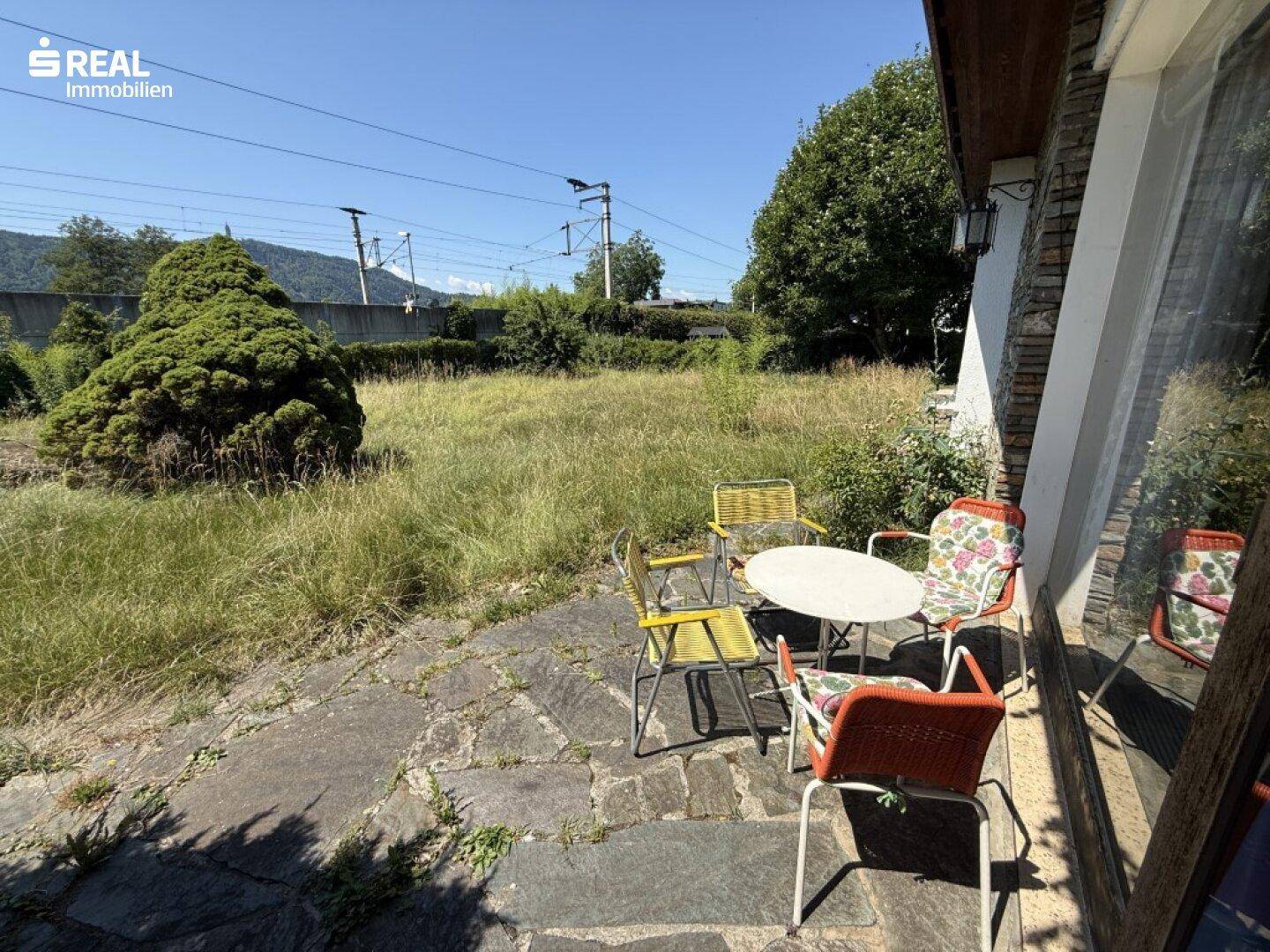 Kleine gepflasterte Terrasse mit Gartenmöbeln und Blick ins Grüne.