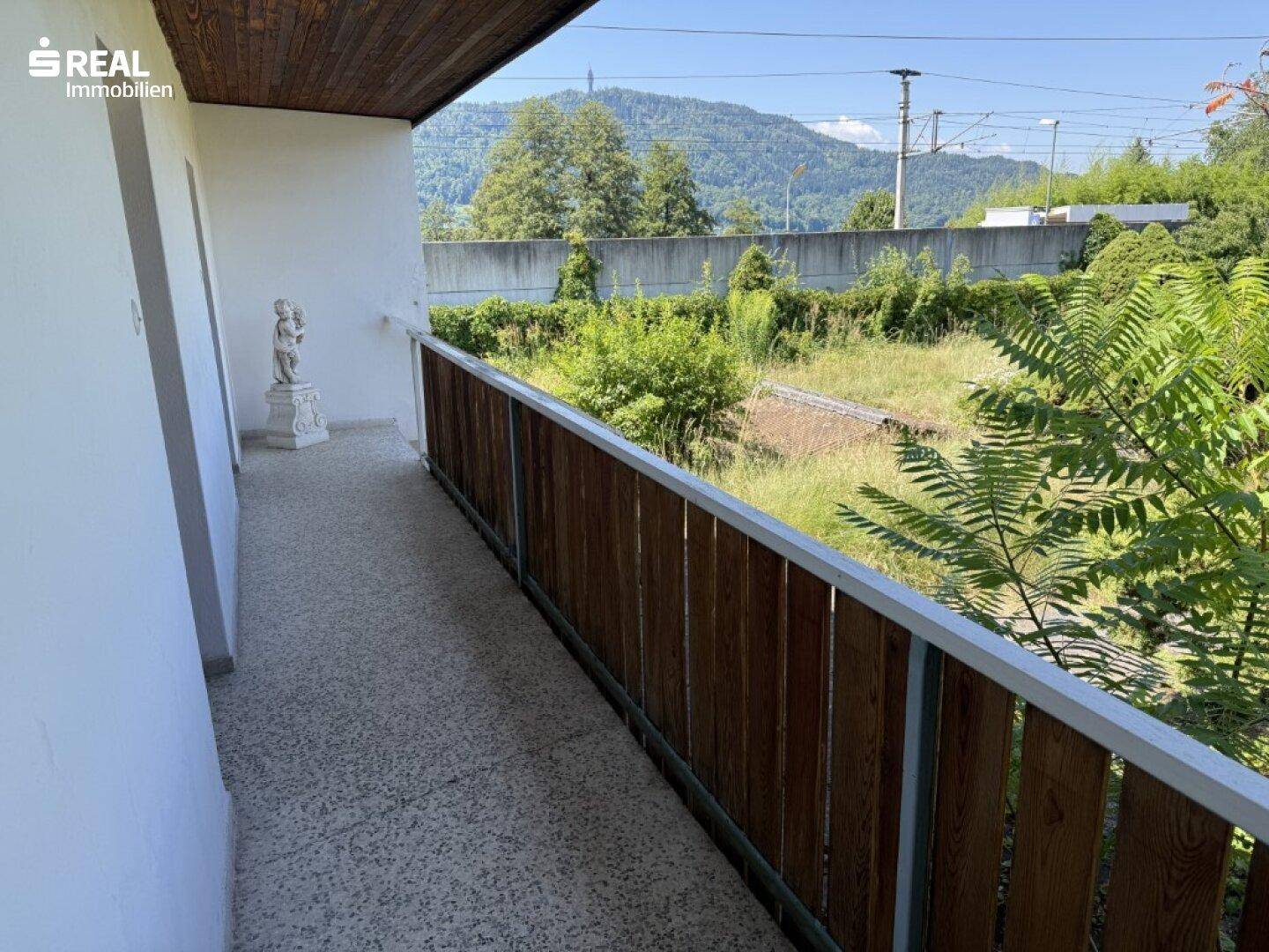 Langer Balkon mit Holzgeländer und Blick auf die umliegende Landschaft und Berge.