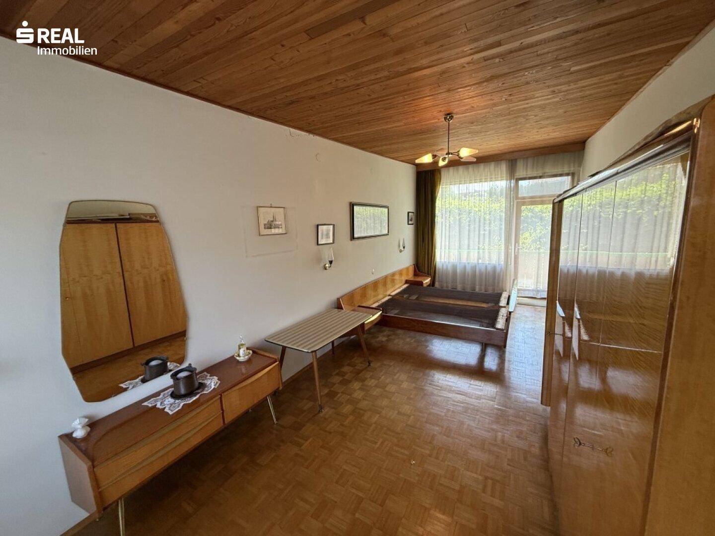 Schlafzimmer mit Holzdecke, Parkettboden und Vintage-Möbeln, hell durch große Fenster.