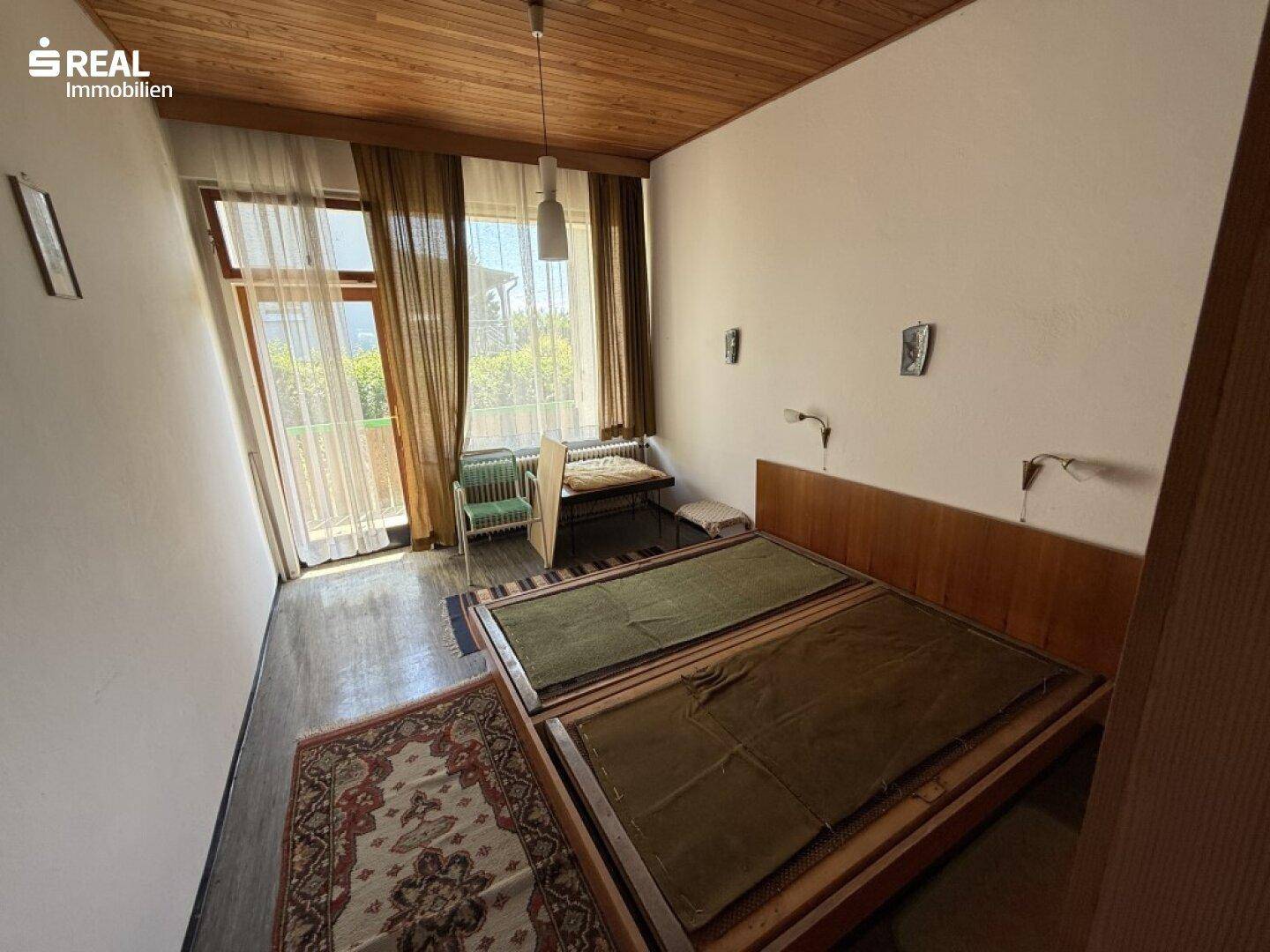 Helles Schlafzimmer mit Holzdecke, Parkettboden und Zugang zu einem Außenbereich.