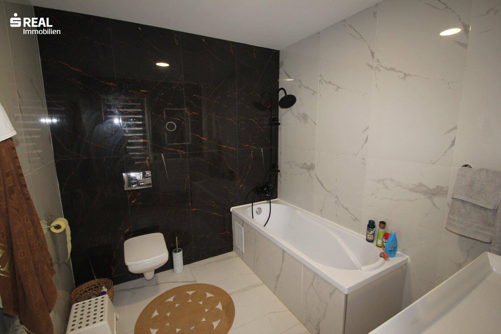 Modernes Badezimmer mit dunklen und hellen Marmorfliesen, Badewanne und Dusche.