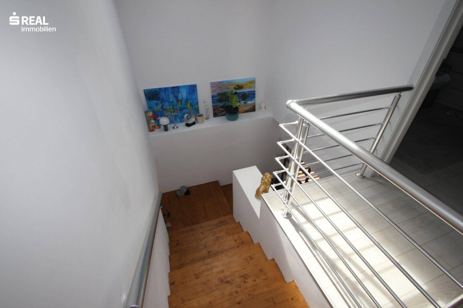 Treppenhaus mit Holzstufen und modernem Edelstahlgeländer, das in den unteren Bereich führt.