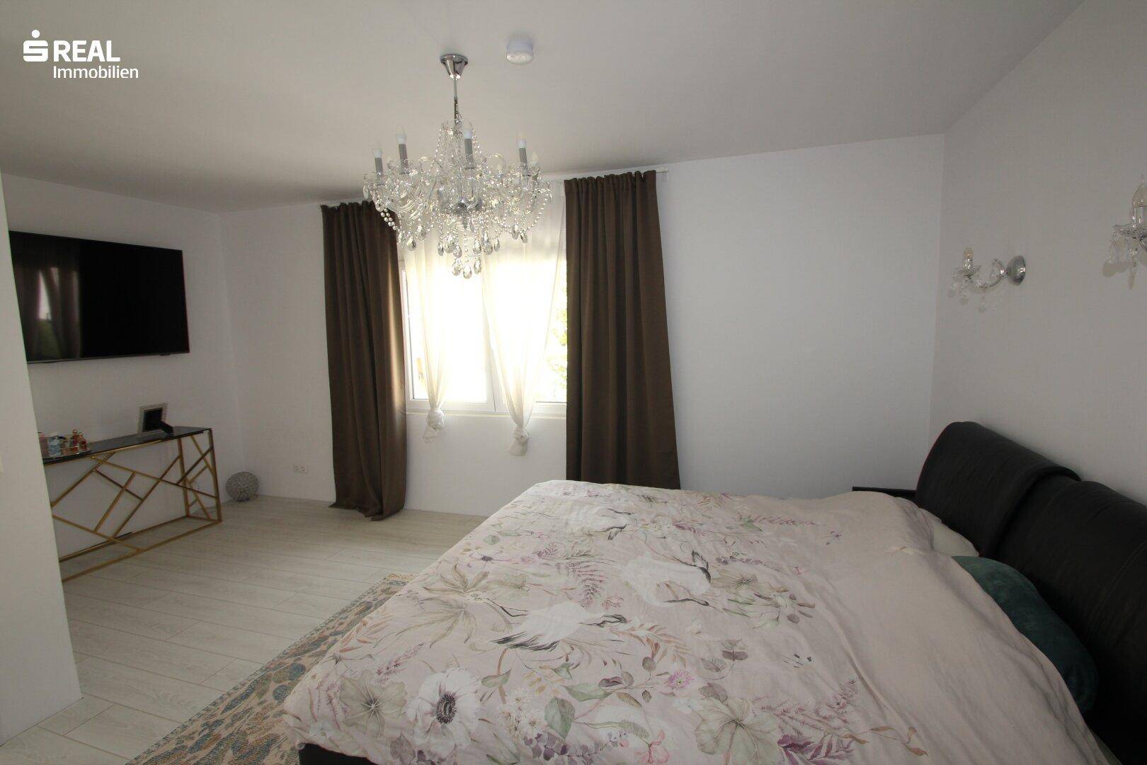 Großes Schlafzimmer mit Doppelbett, Kronleuchter und braunen Vorhängen, hell und einladend.