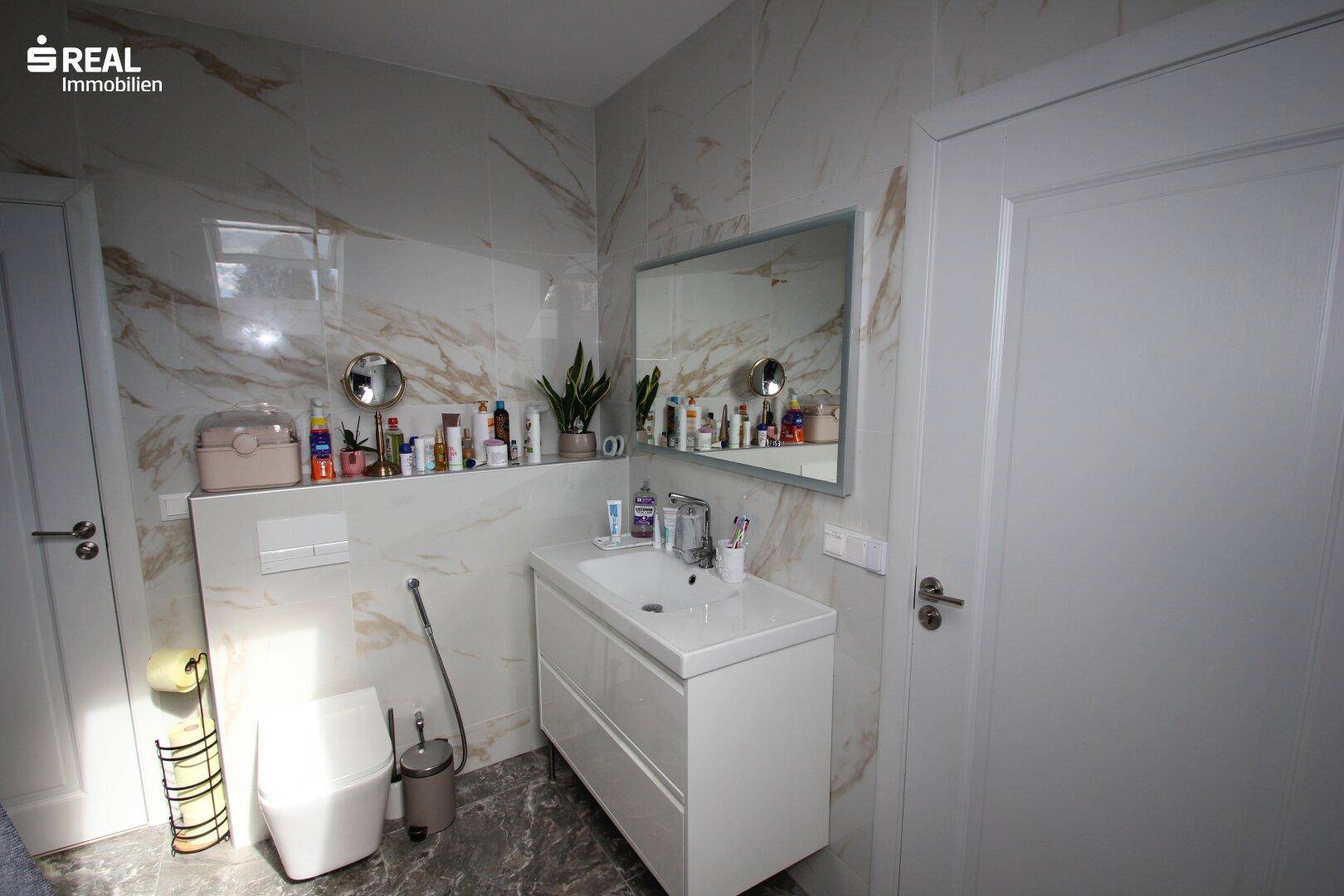 Helles Badezimmer mit Waschtisch, Toilette und Marmorfliesen unter einer Dachschräge.