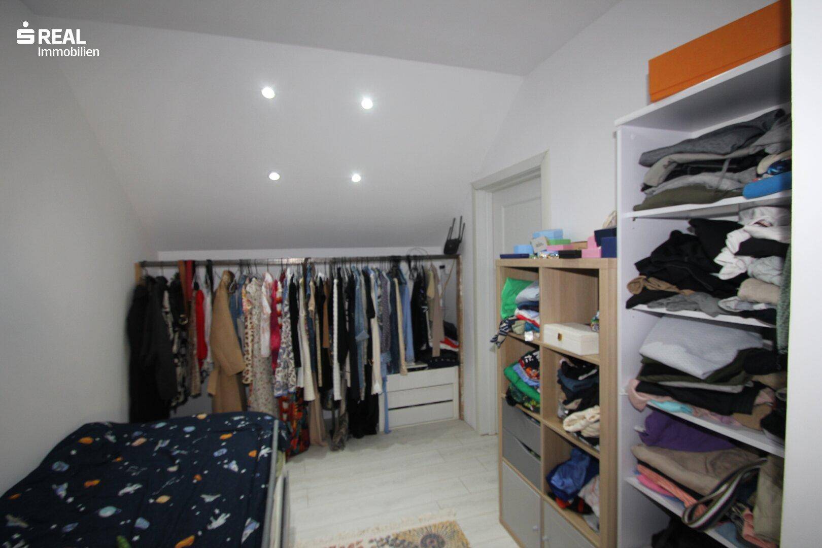 Ankleidezimmer mit offener Kleiderstange und Regalen unter einer Dachschräge.