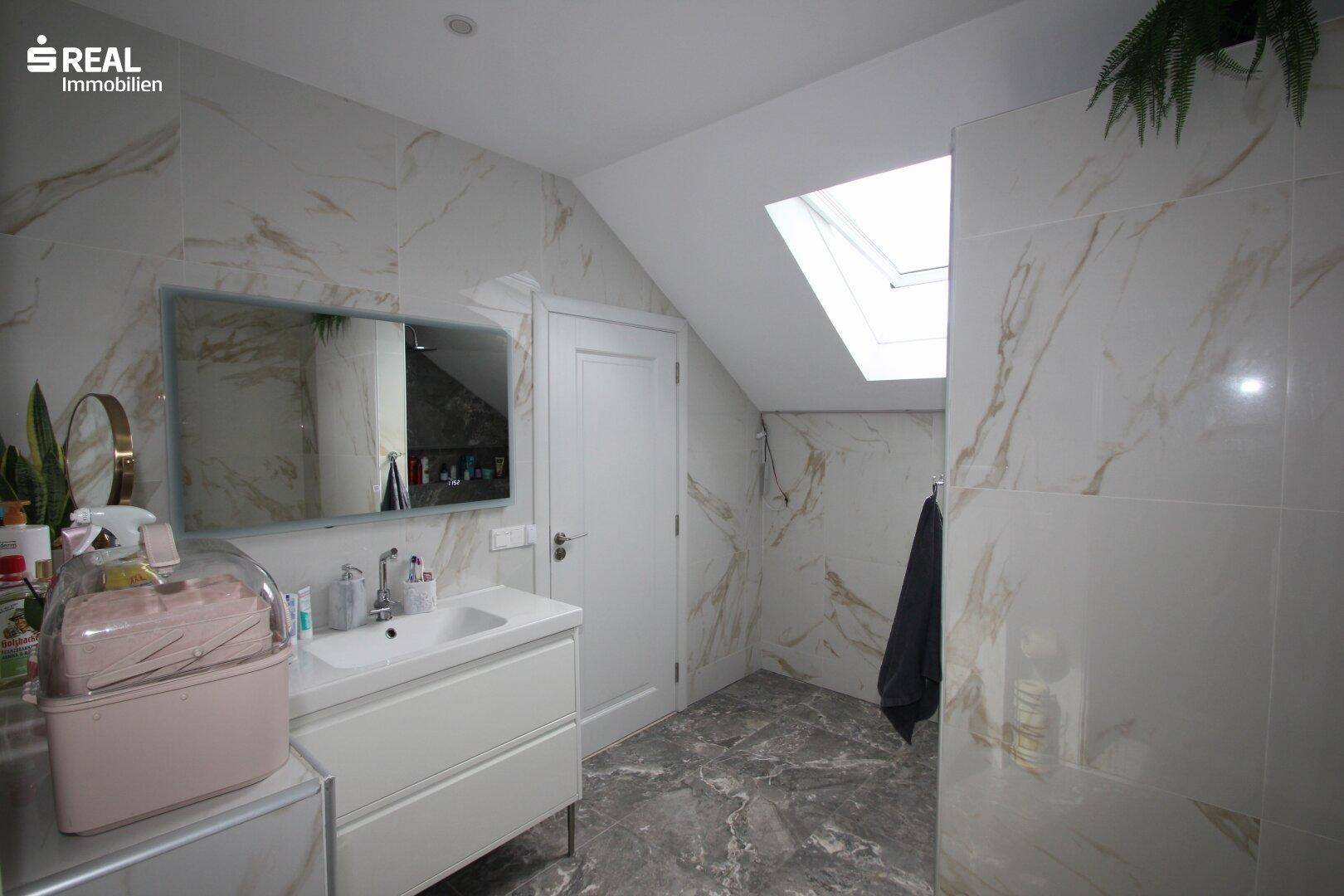 Modernes Badezimmer mit Marmorfliesen, Waschtisch und Dachfenster für natürliches Licht.