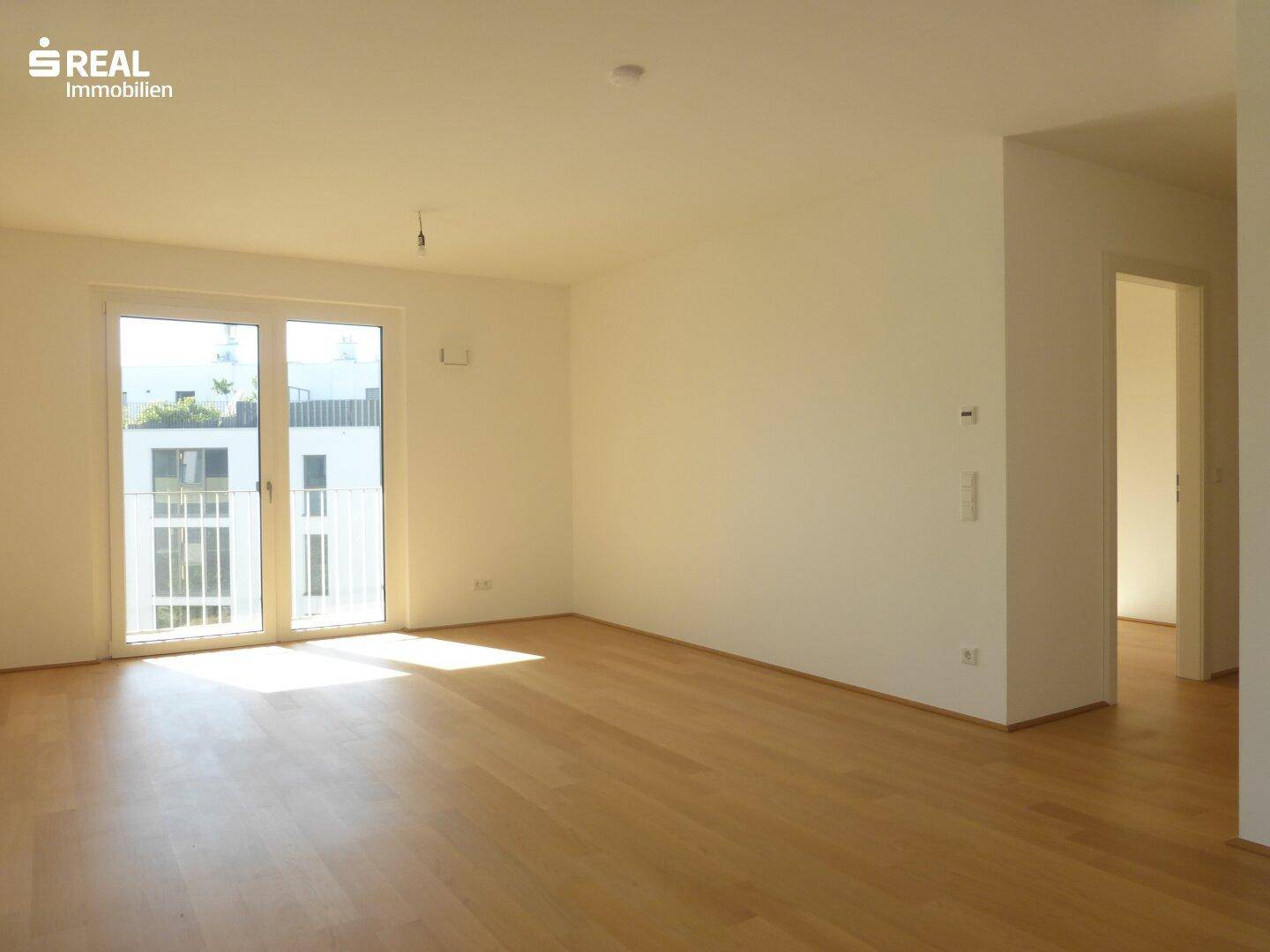 Geräumiges Wohnzimmer mit hellem Parkettboden und Zugang zu einem französischen Balkon.