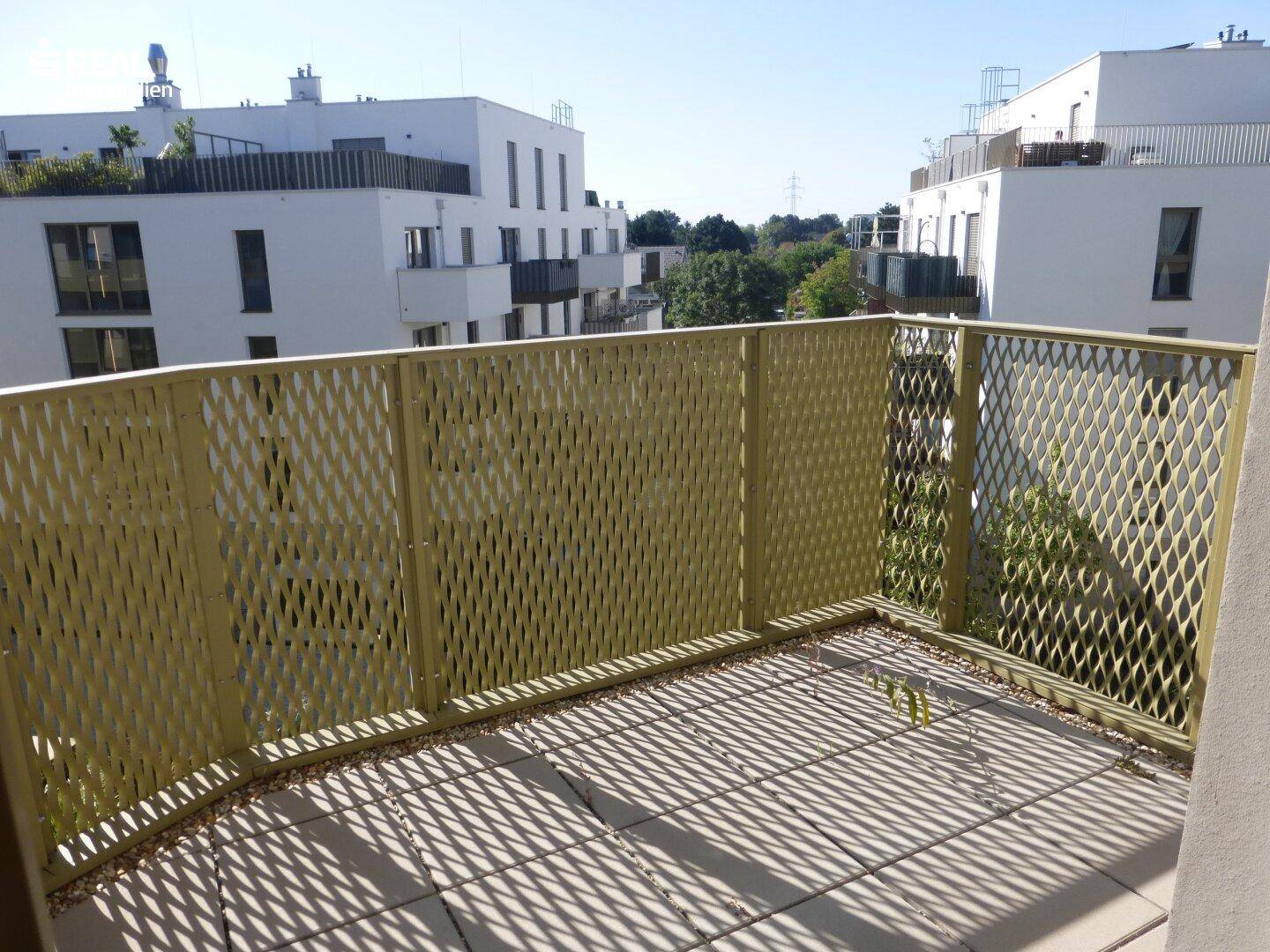 Geräumiger Balkon mit Fliesenboden und perforiertem Metallgeländer an einem modernen Gebäude.