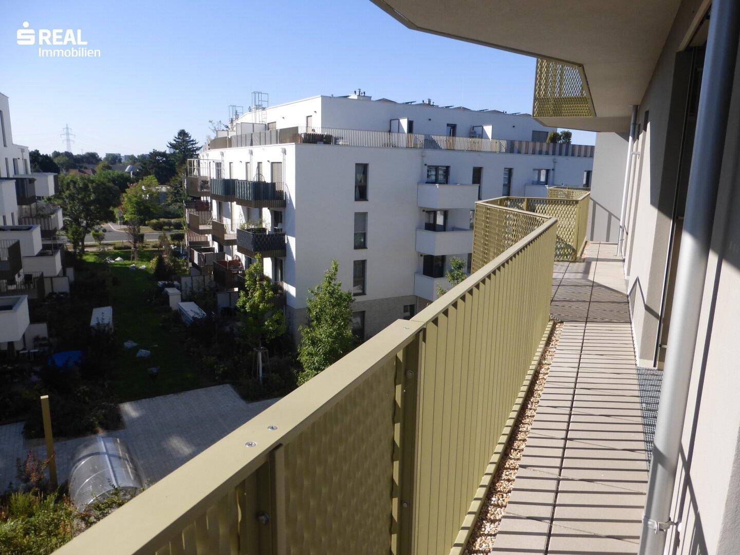 Langer Balkon mit Gittergeländer und weitem Blick auf die Wohnanlage mit Grünflächen.