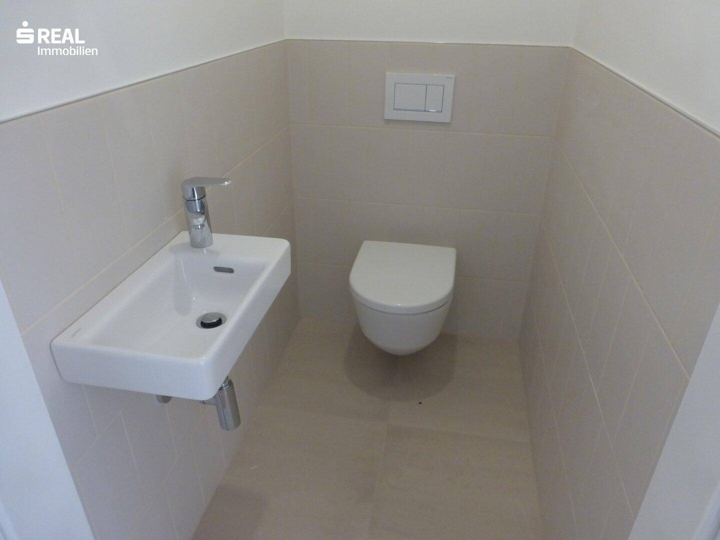 Gäste-WC mit wandhängender Toilette und kleinem Waschbecken in minimalistischem Design.