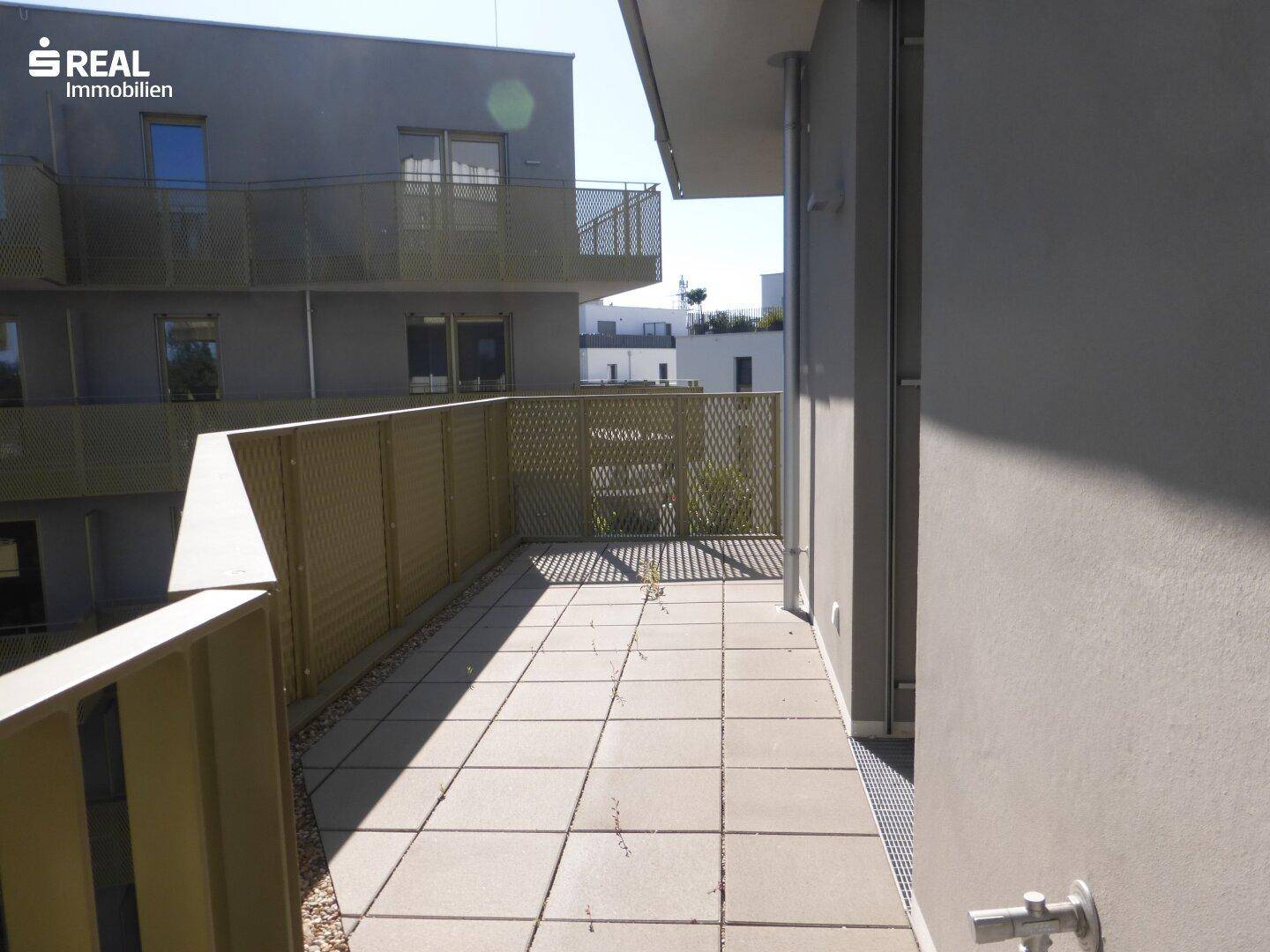 Geräumiger Balkon mit Fliesenboden und Blick auf die umliegenden Gebäude.