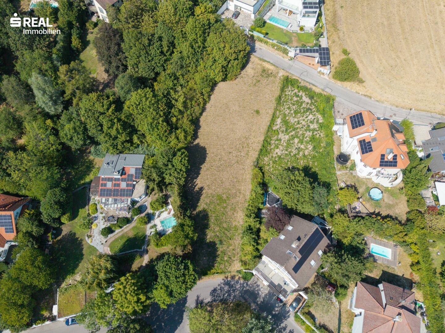 Übersicht aus der Vogelperspektive auf das Grundstück, umgeben von grüner Natur und Häusern mit Pools.