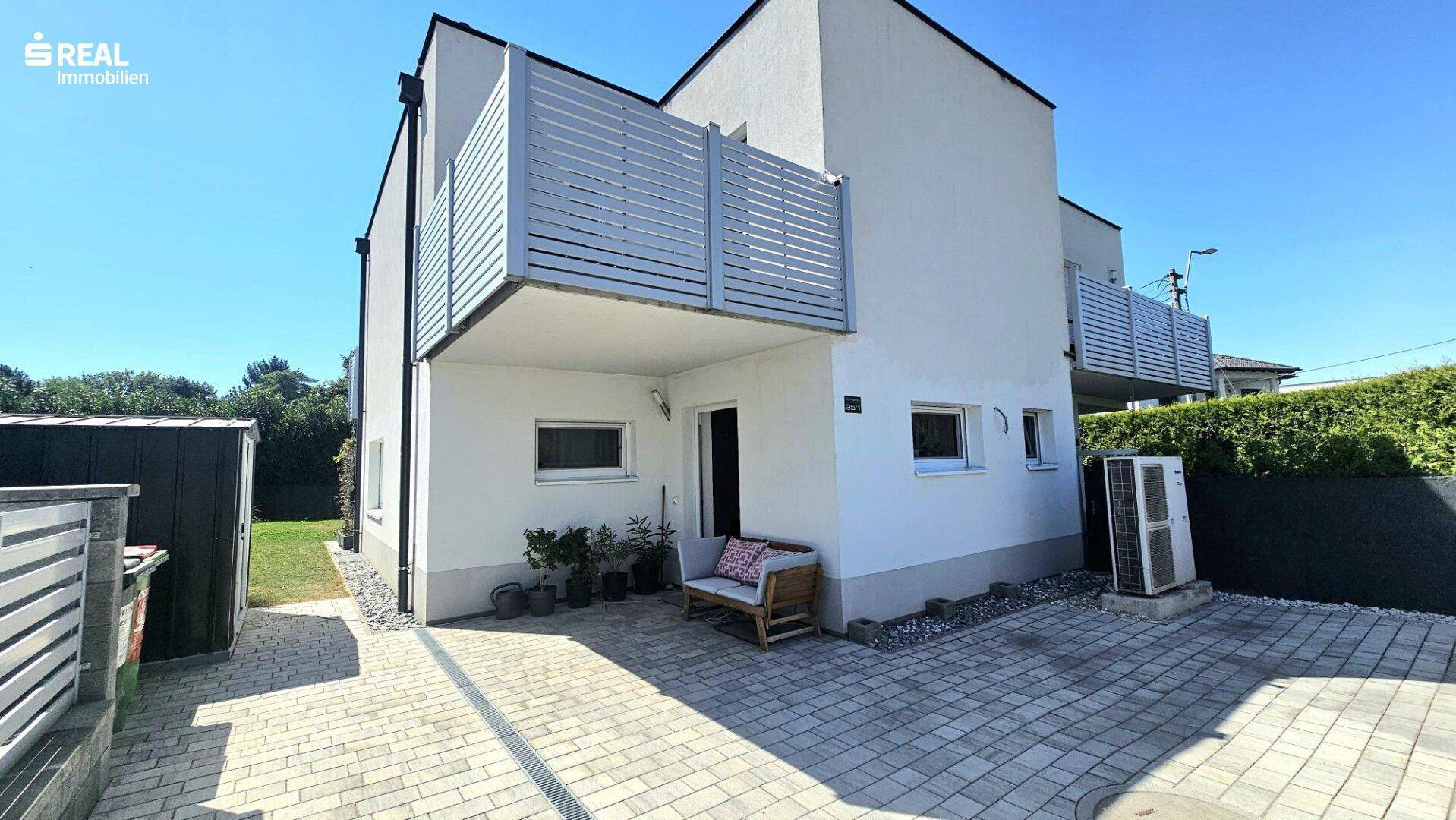 Rückseite des modernen Reihenhauses mit gepflastertem Bereich und Klimaanlage.