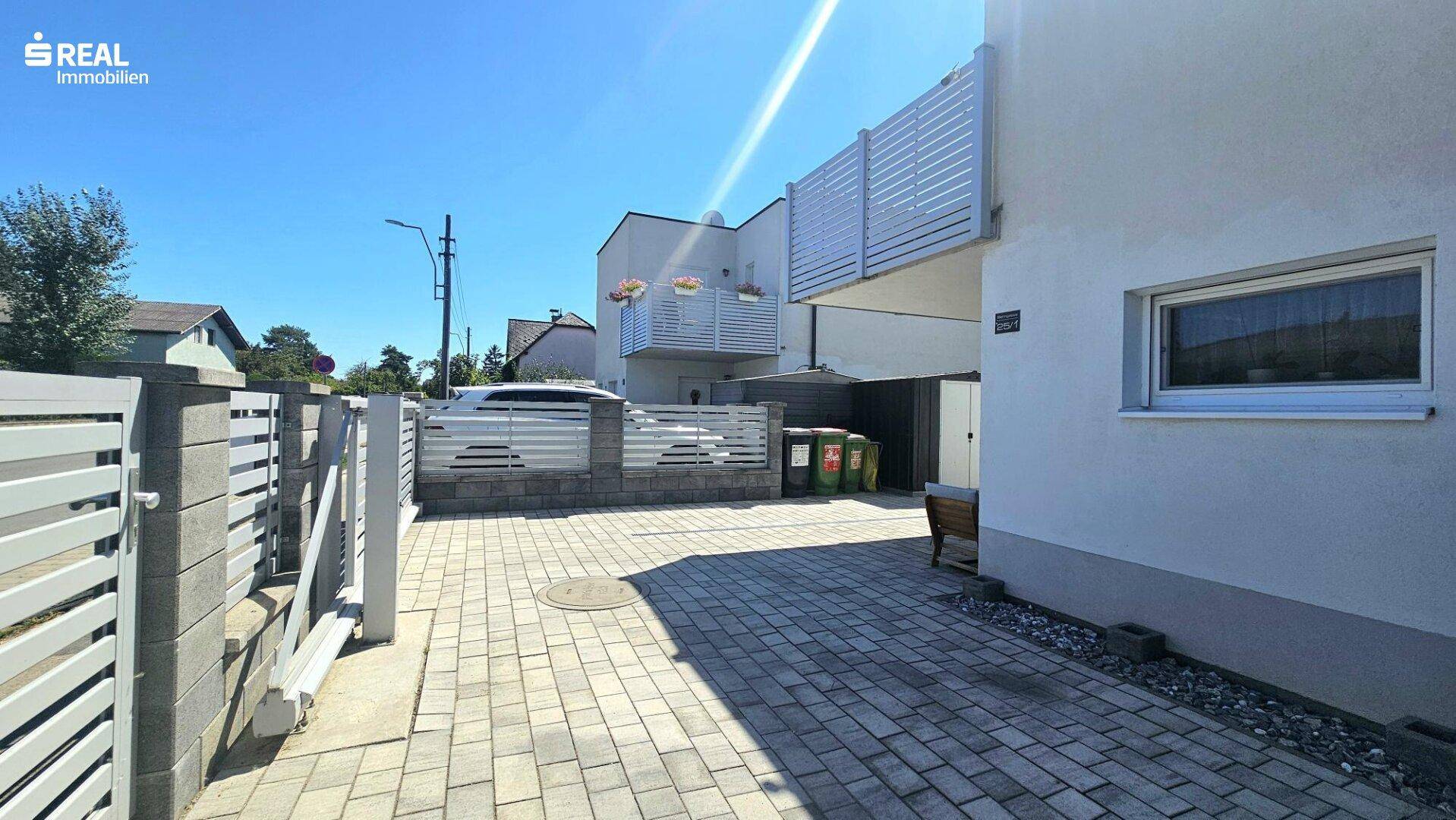 Zufahrt zum Reihenhaus mit gepflastertem Parkplatz und modernem Zaun.