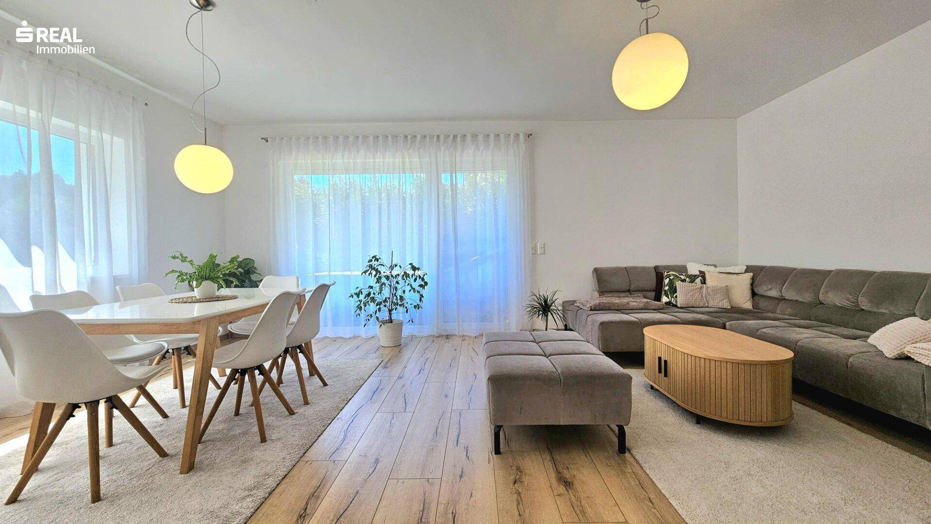 Heller Wohn- und Essbereich mit modernem Holzboden, großem Esstisch und bequemer Couch.