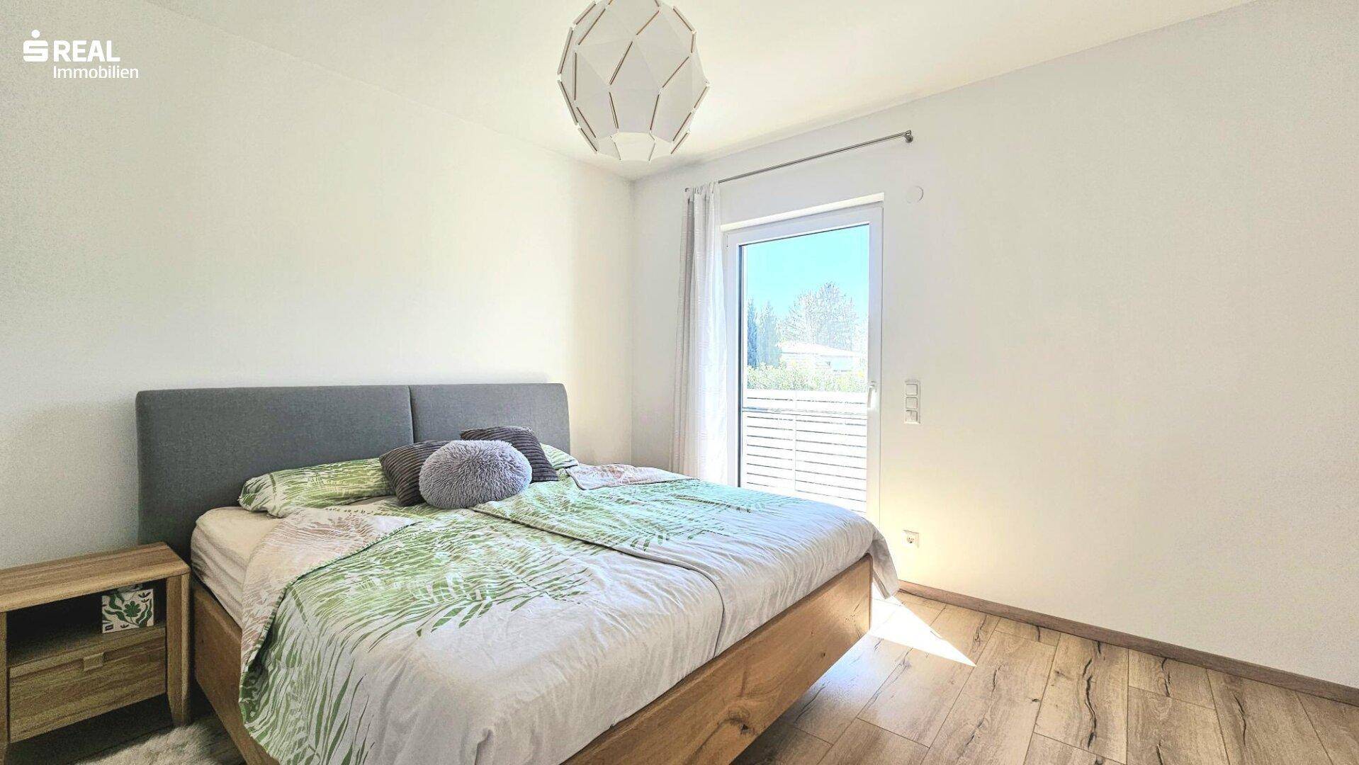 Helles Schlafzimmer mit Holzbett, Nachttisch und Zugang zum Balkon.