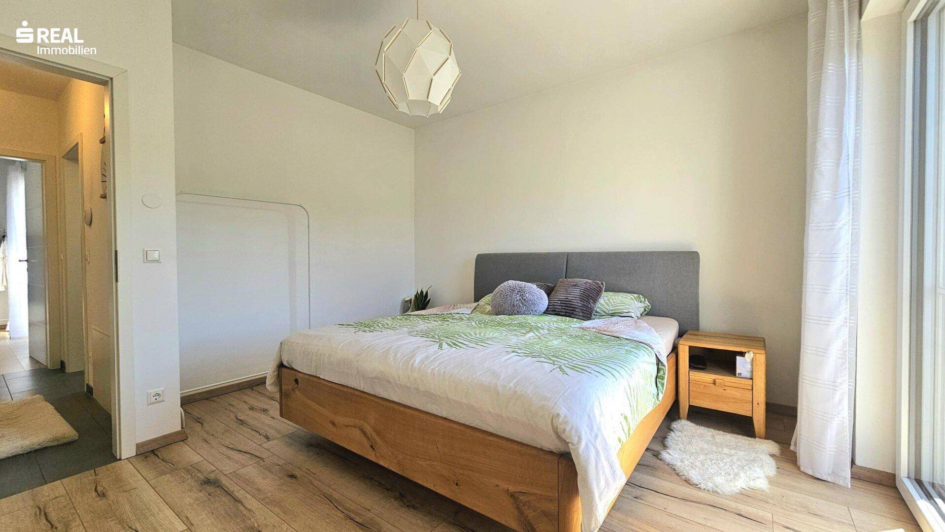 Geräumiges Schlafzimmer mit Holzboden, Doppelbett und viel Tageslicht.