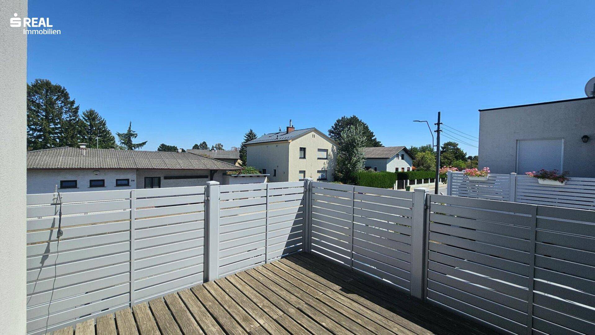 Großer Balkon mit Holzboden und moderner Sichtschutzwand, ideal zum Entspannen.